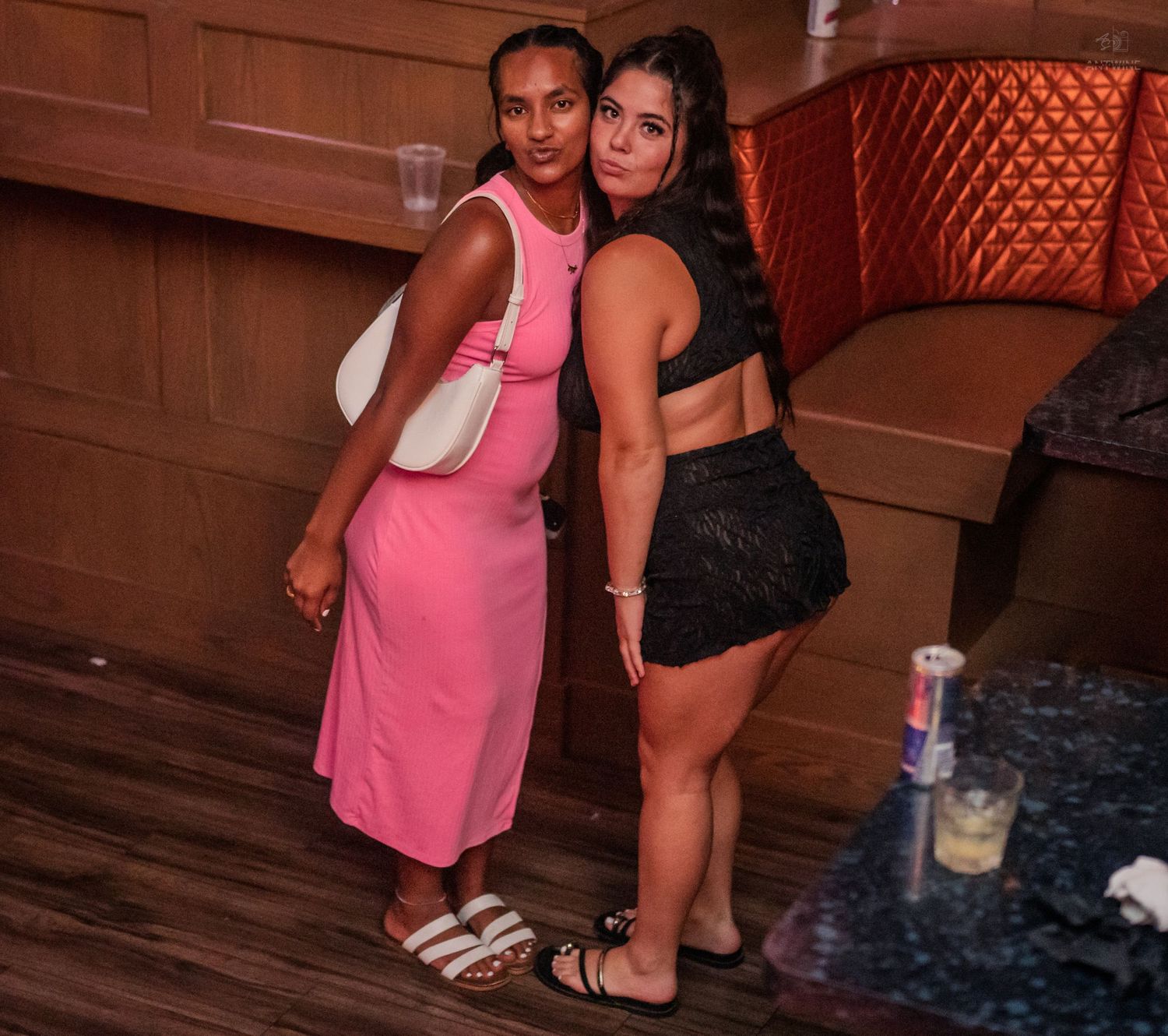 Two young women posing together smiling at a bar or nightclub venue.