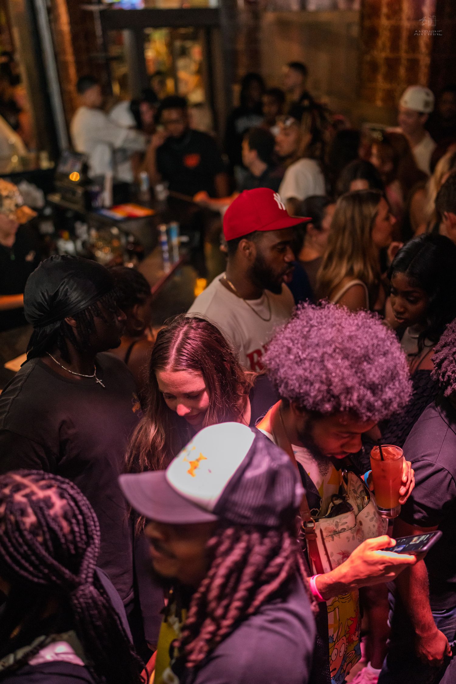 Diverse group of partygoers mingling under purple lighting at a busy nightclub event.