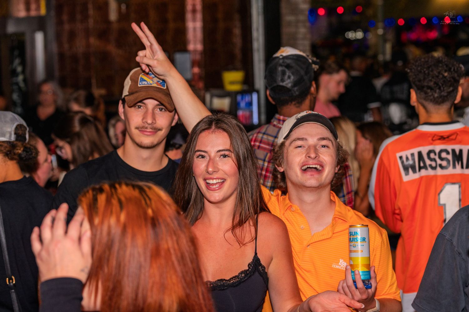 Three friends smile and pose together in a crowded outdoor nightlife street event.