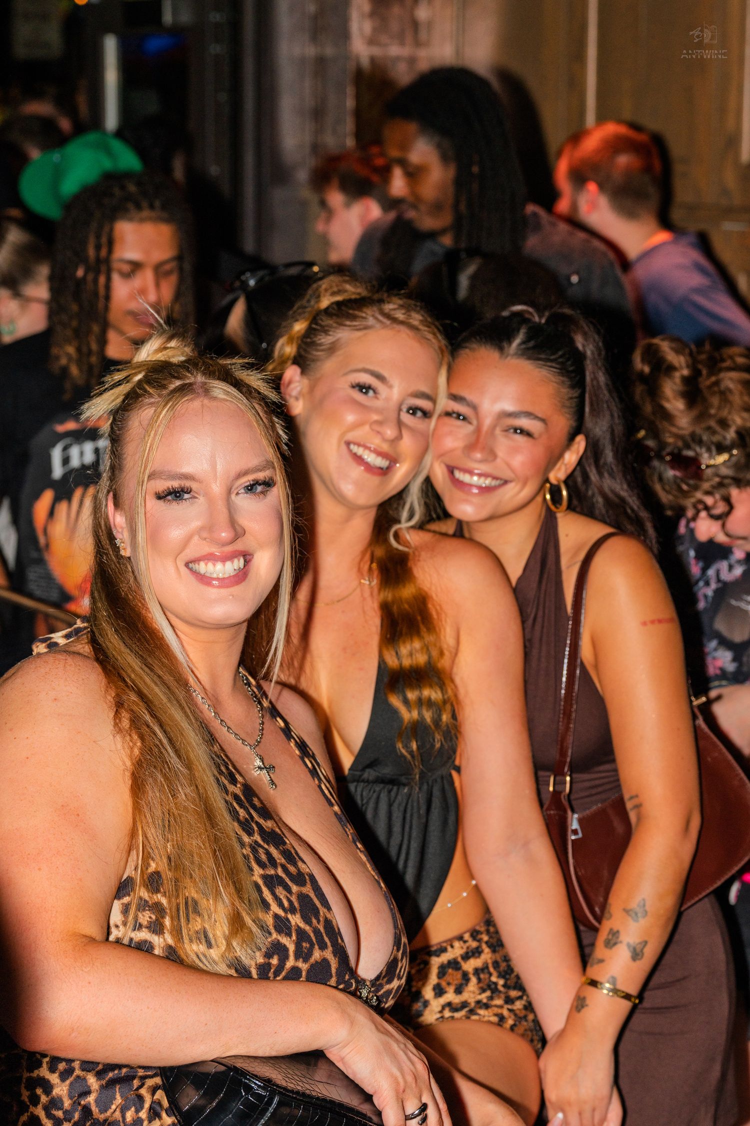 Three smiling young women posing together at a nightclub event.