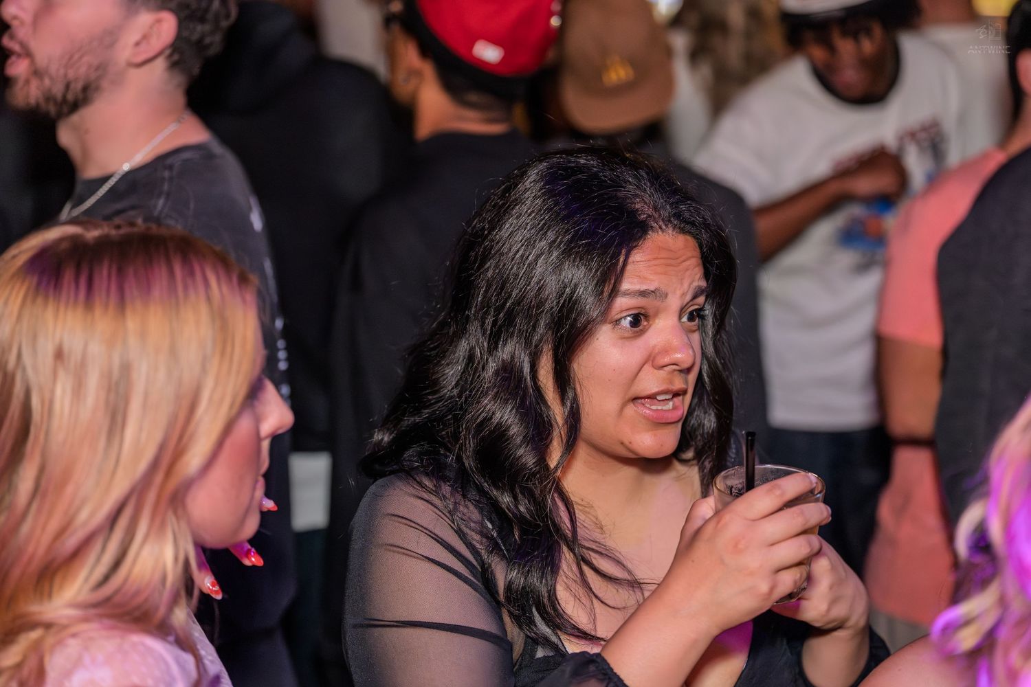 A woman with dark hair talks animatedly while holding a drink at a nightclub.