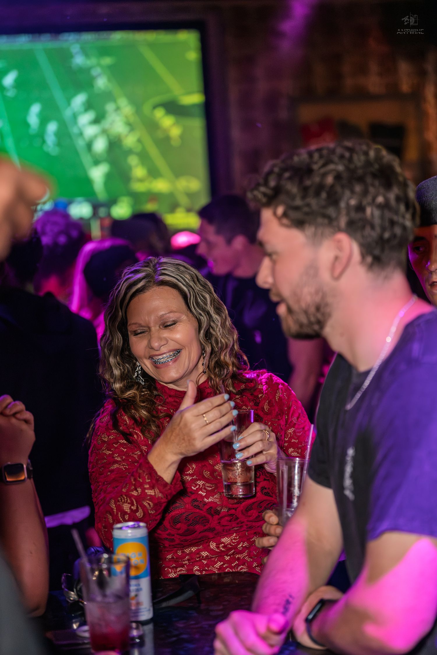 Smiling woman in red lace top giving thumbs up while chatting at a nightclub bar.