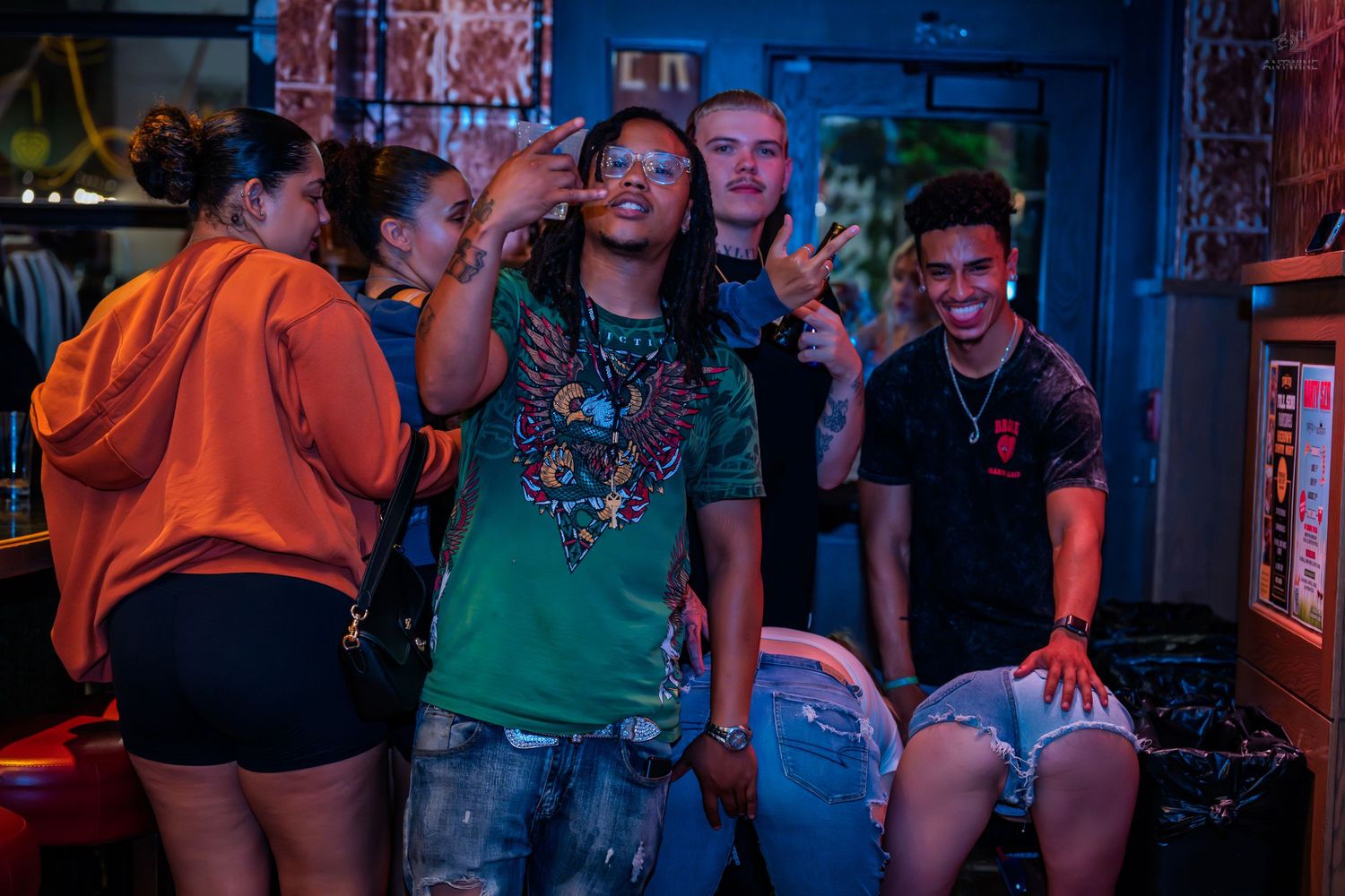 Group of friends posing and having fun at a vibrant nightclub party with colorful lighting.