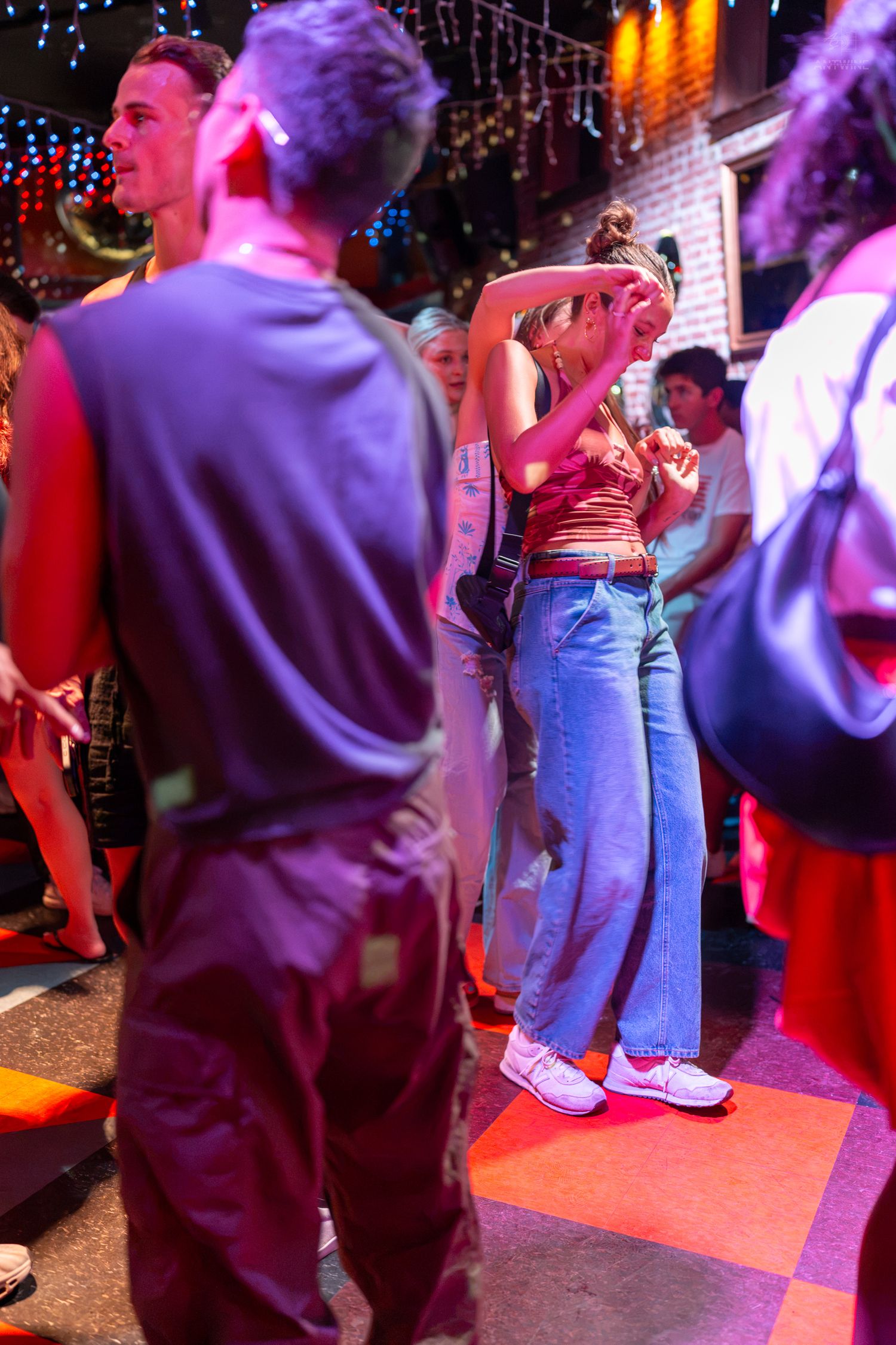 People dancing at a vibrant nightclub with colorful red and blue lighting on a checkered dance floor.
