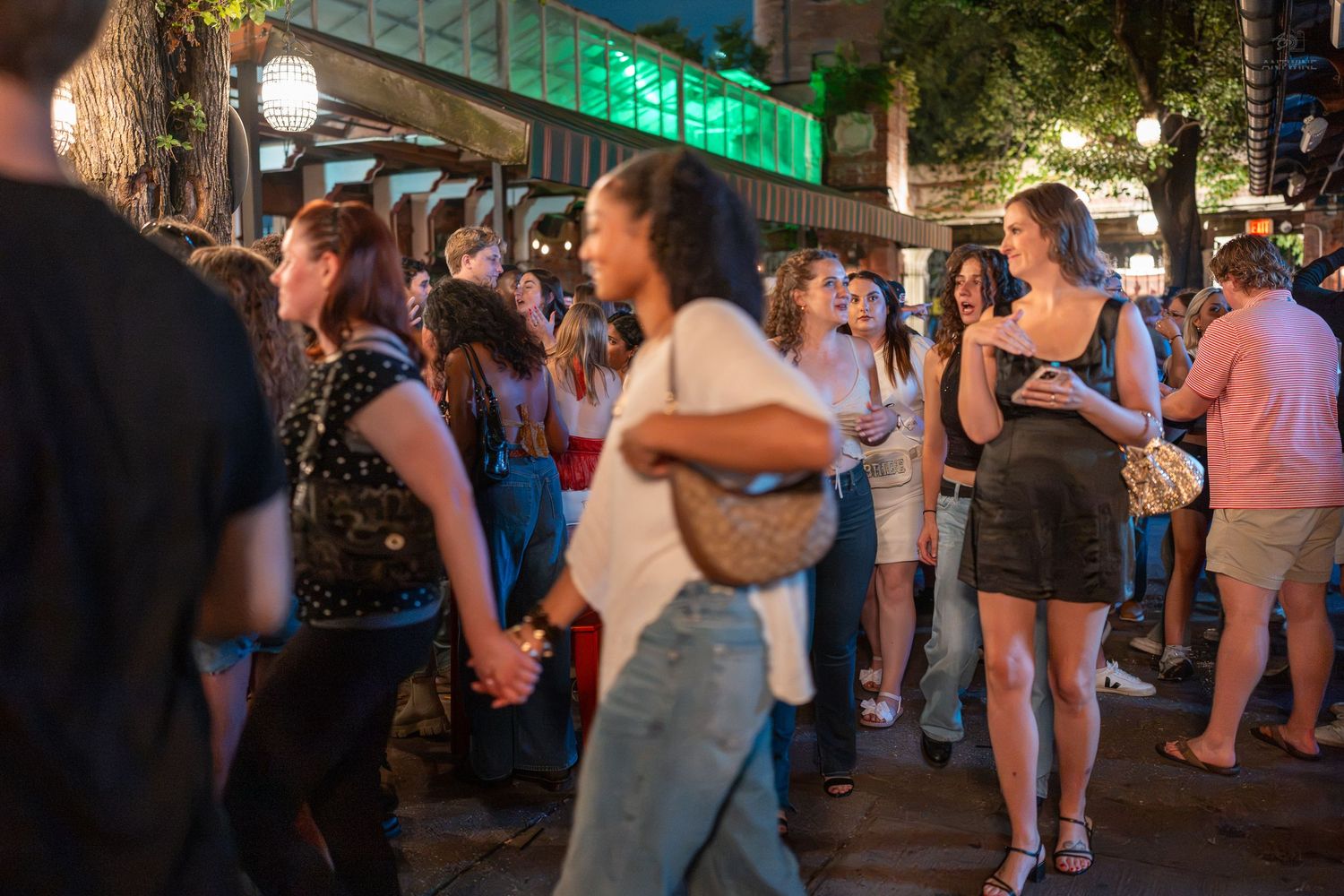 Crowd of young people socializing outdoors at a lively nighttime street event in an urban setting.