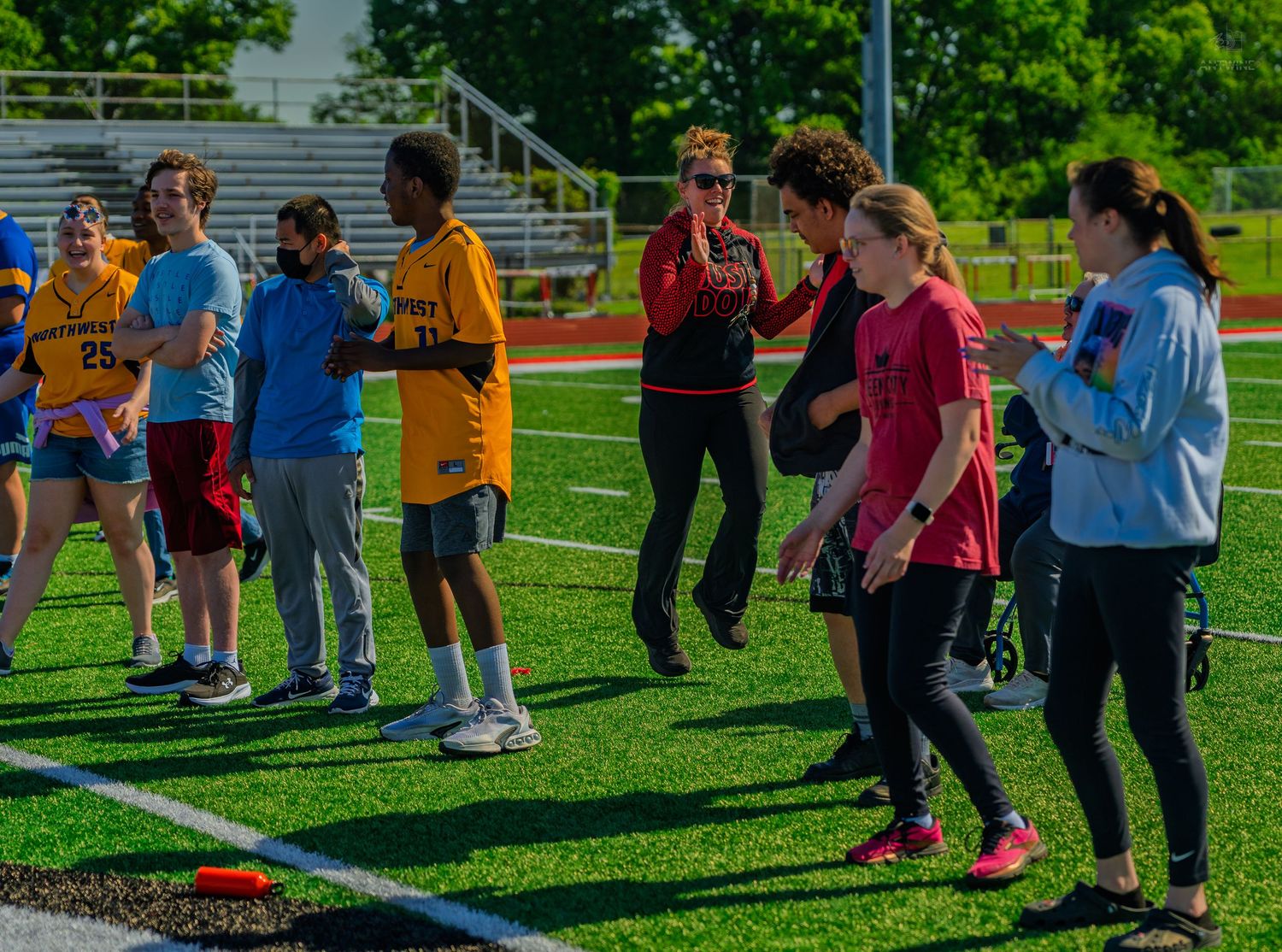 Students participate in an outdoor field day activity on a green turf sports field on a sunny day.