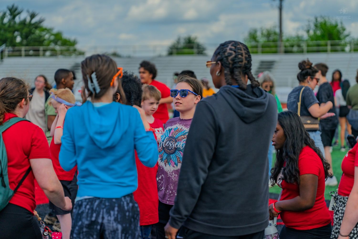 Diverse group of people gathered outdoors at a community event on a green sports field under cloudy skies.