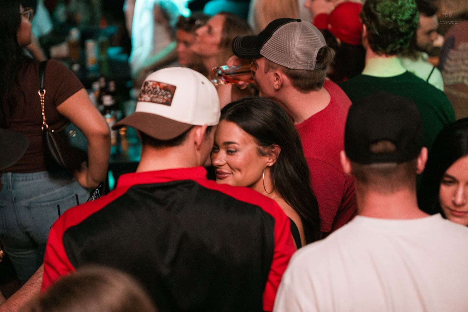 Couple sharing an intimate moment while surrounded by a crowd at a busy bar event.
