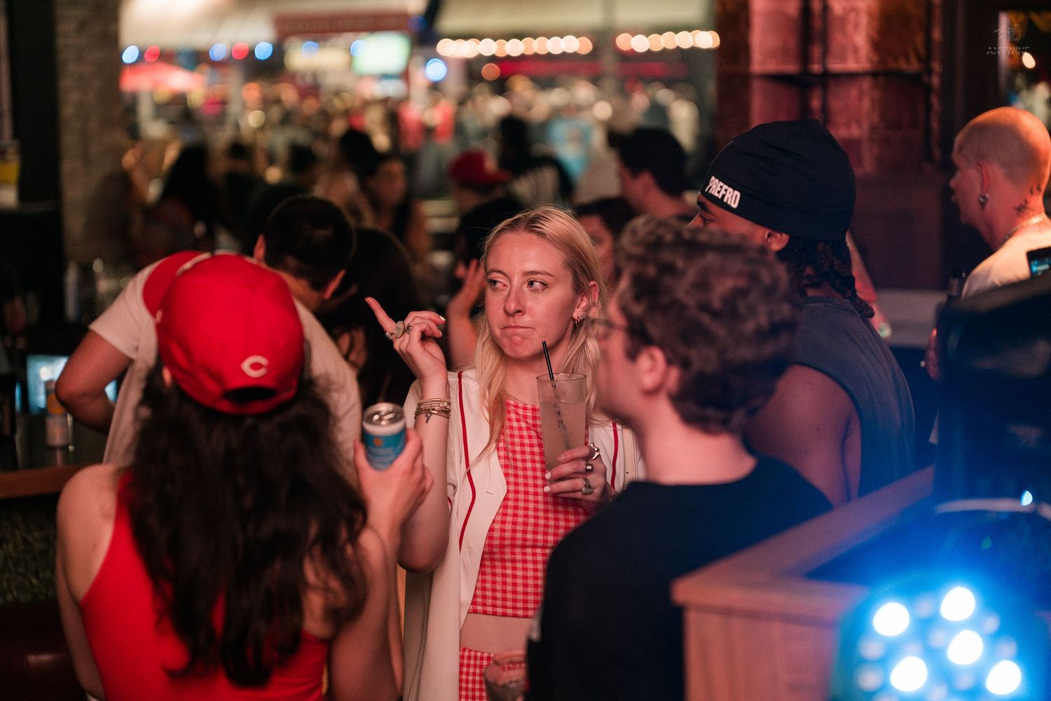 Young woman in checkered outfit socializing with friends at a crowded bar.