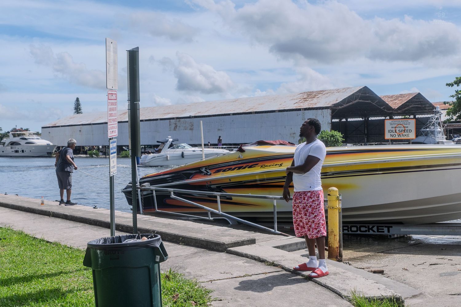 Person standing on dock observing colorful racing boats near a waterfront marina storage building.