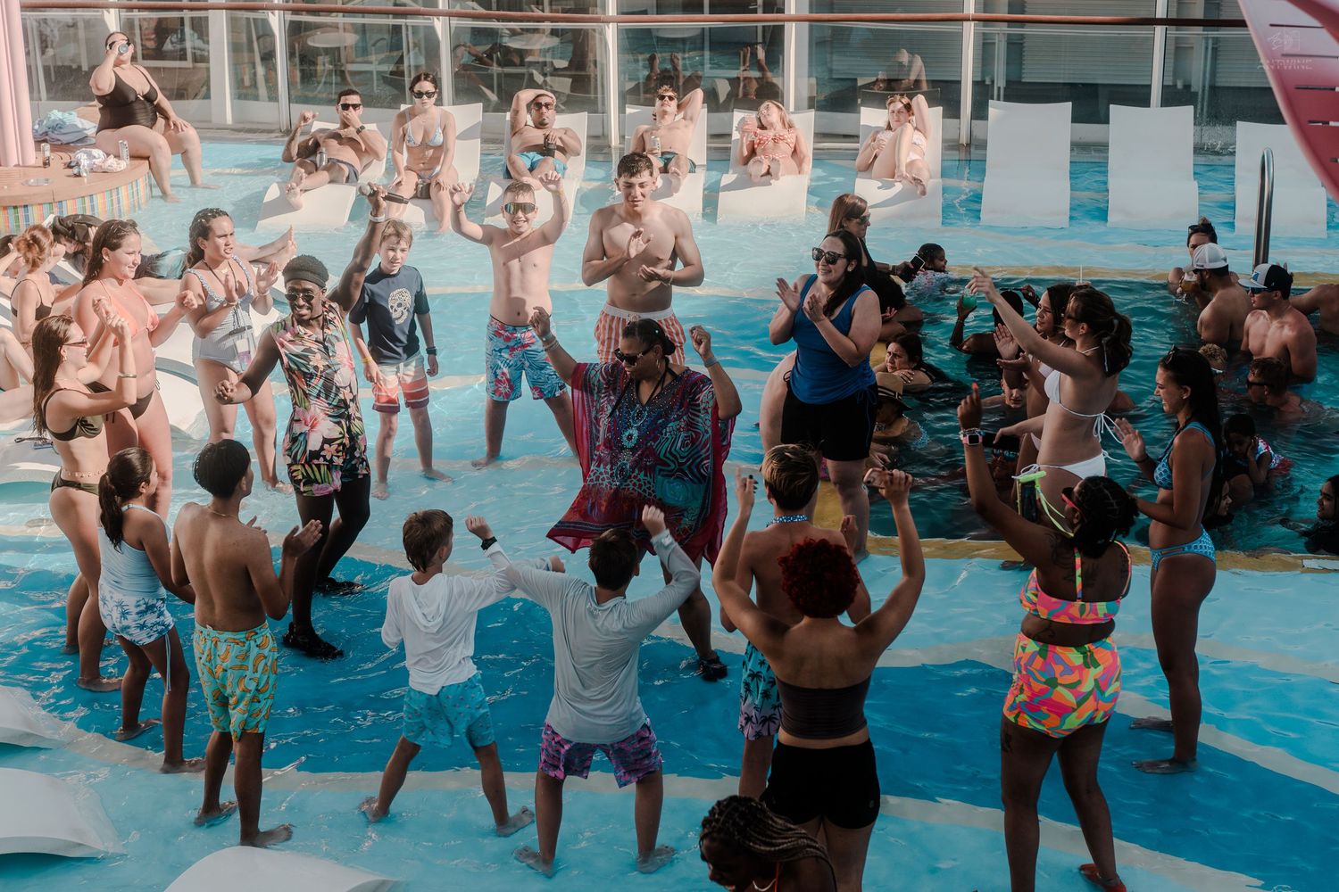 Lively pool party with guests dancing and celebrating in swimwear at an outdoor cruise ship pool.