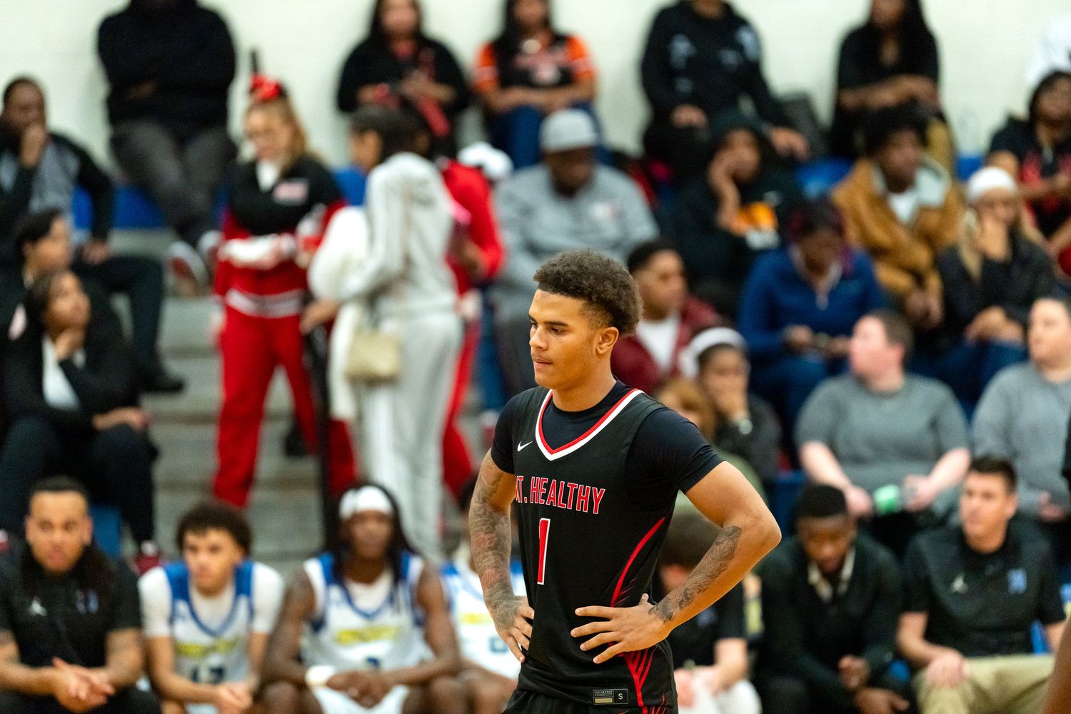 Basketball player in red uniform number 1 stands with hands on hips during a high school game.