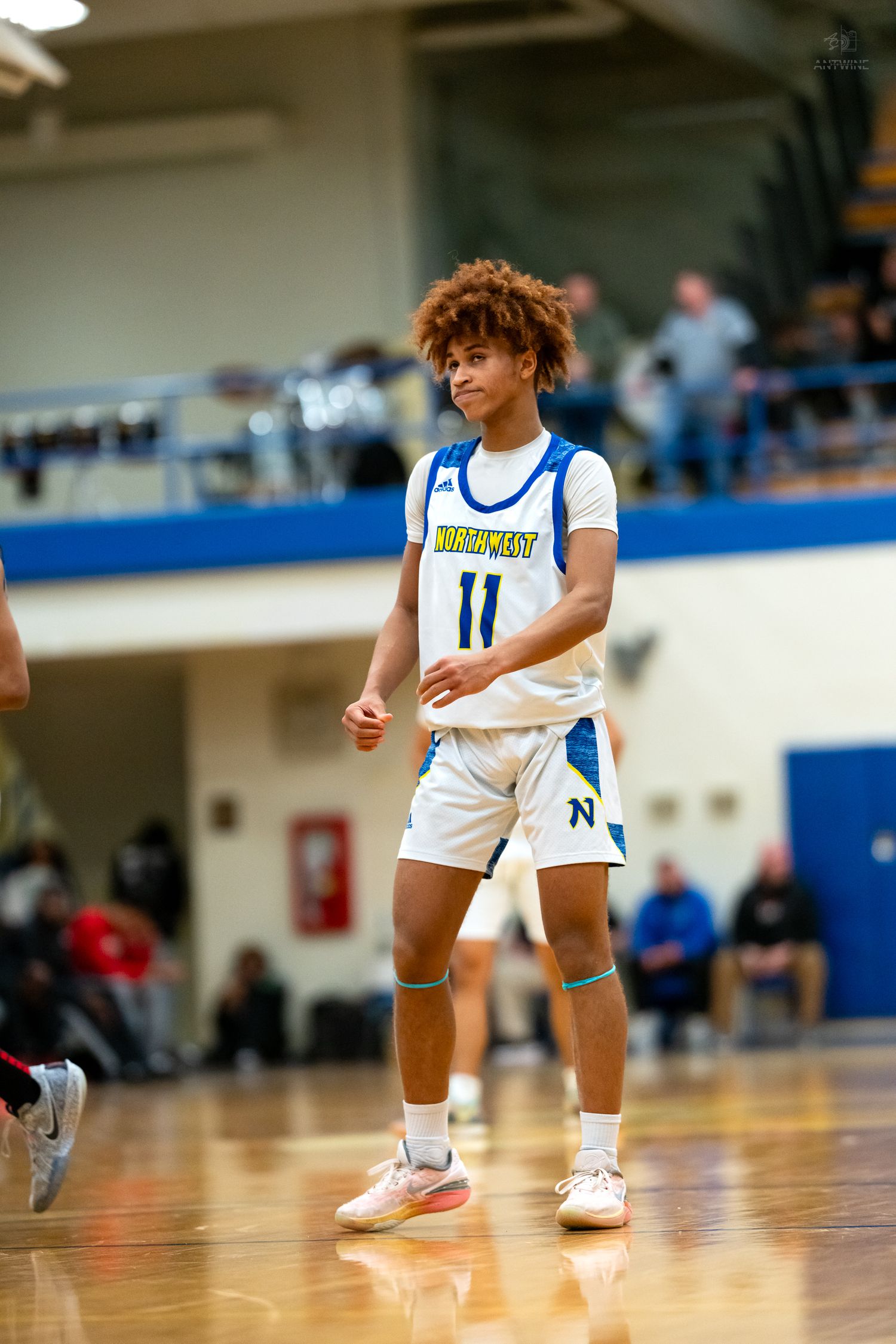 High school basketball player number 11 in Northwest jersey stands ready on polished indoor court.