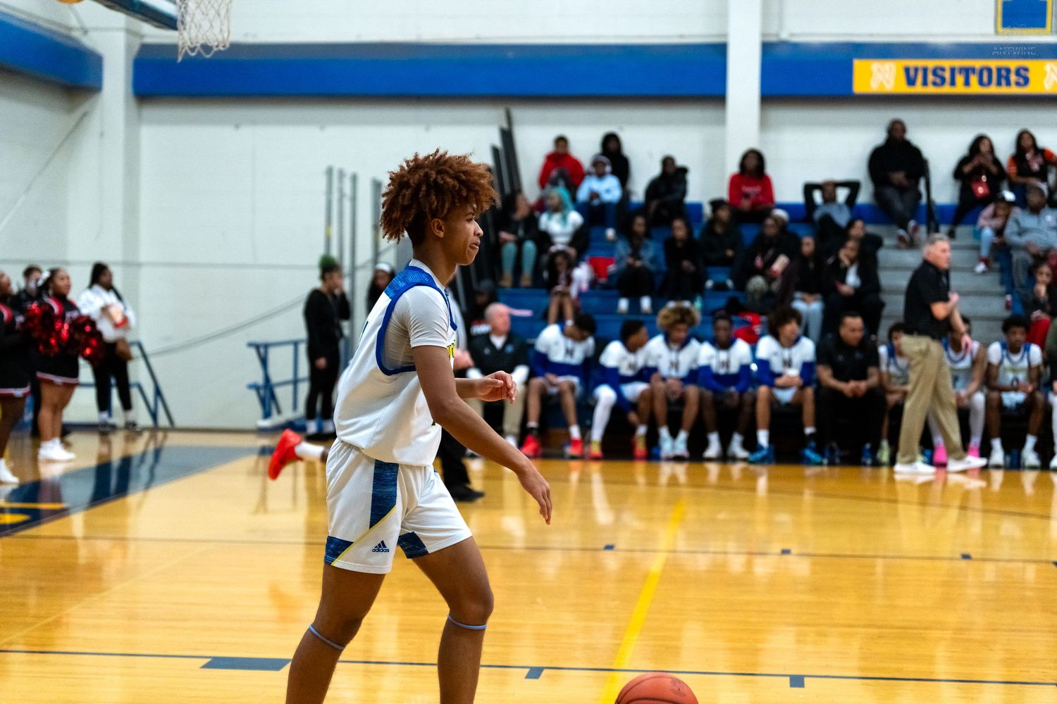 Young basketball player in blue and white uniform dribbles ball during a high school game.