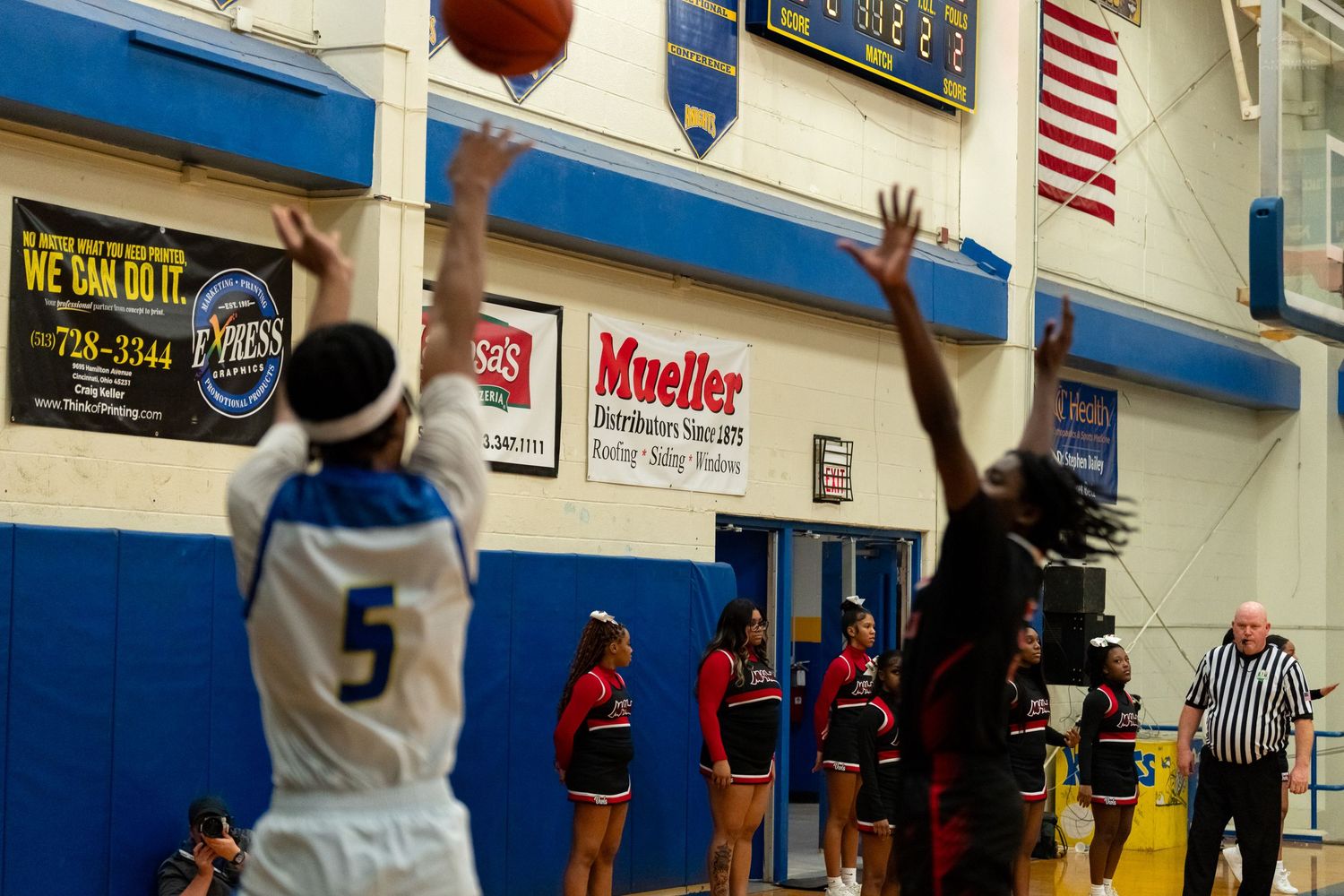 High school basketball player number 5 shoots a jump shot during a gymnasium game.