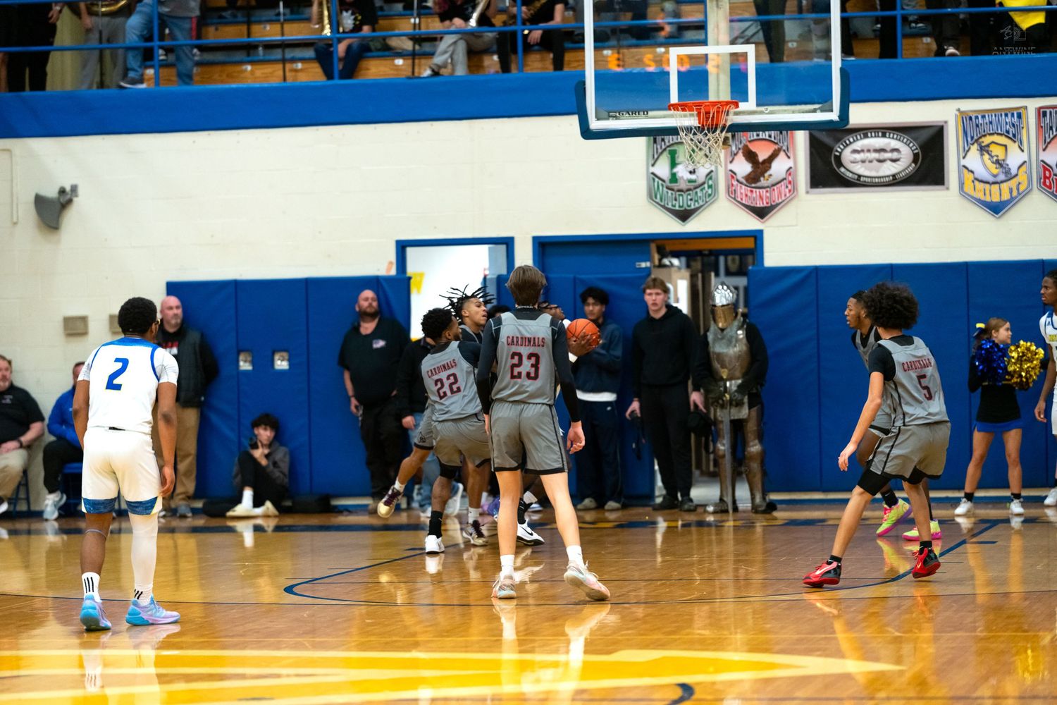 High school basketball players in gray uniforms set up a play near the baseline during an indoor gymnasium game.