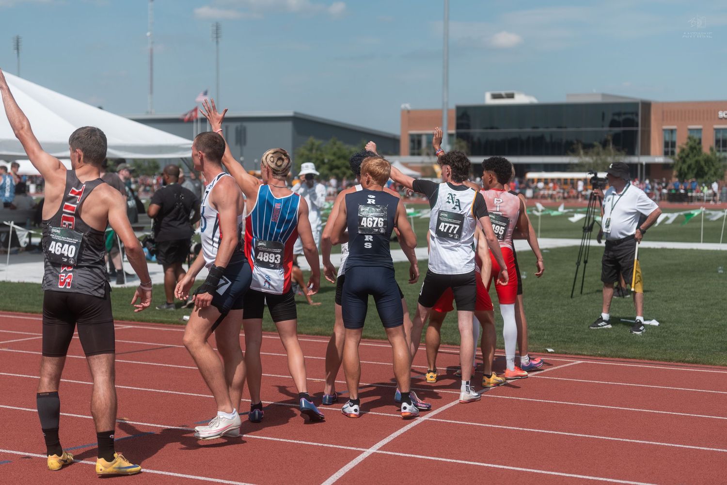 Track and field athletes gather and celebrate on red track after completing relay race at championship meet.