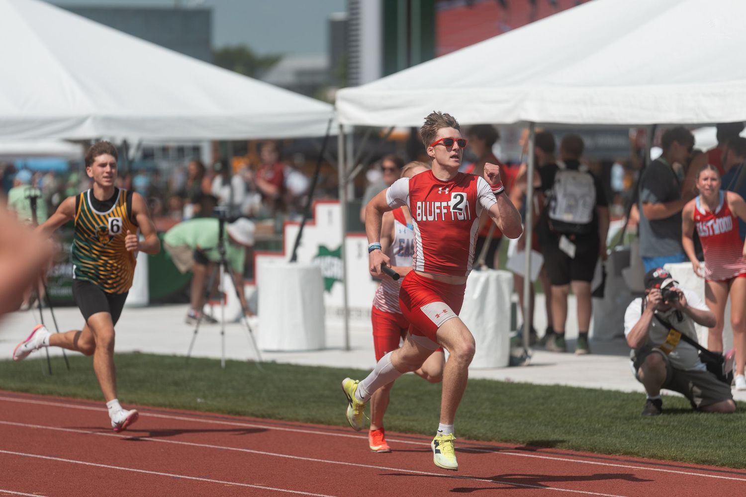 A runner in a red Clippers uniform sprints past competitors during an outdoor track and field meet.