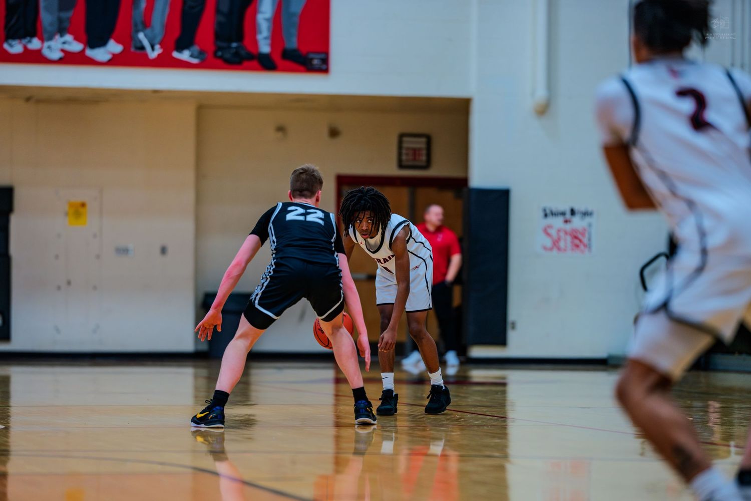 High school basketball player in white uniform dribbles past defender #22 in black during indoor game.