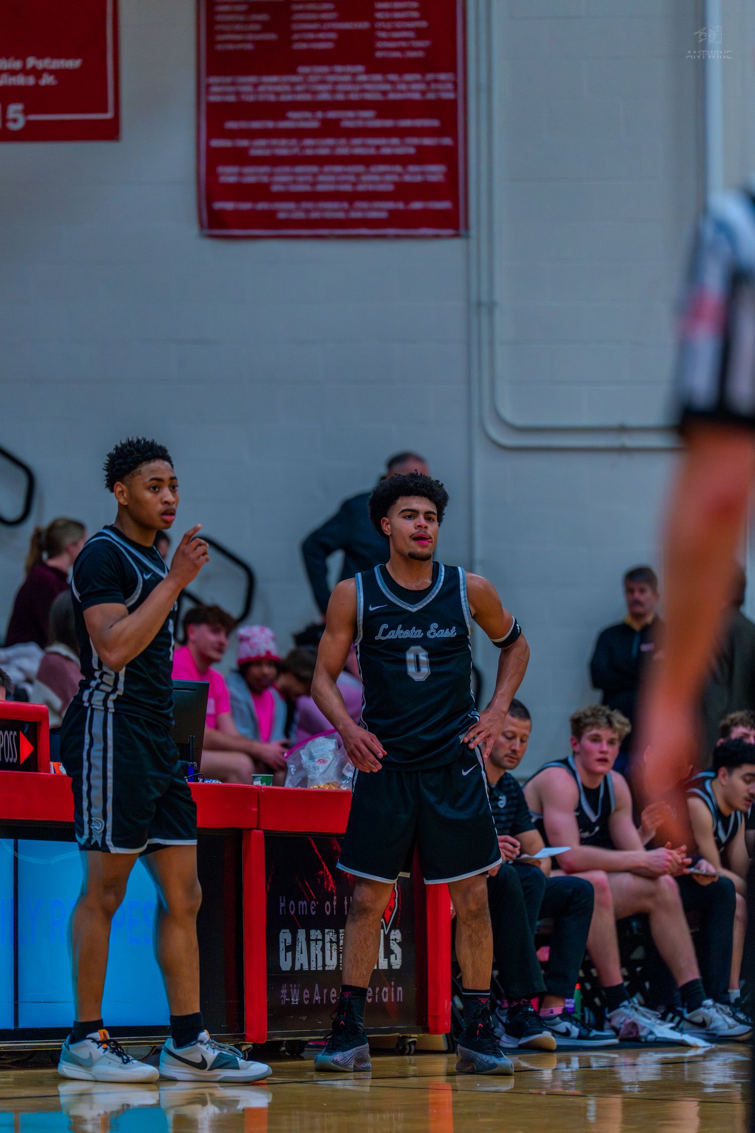 Two Lakota East basketball players stand near the bench during a high school game.