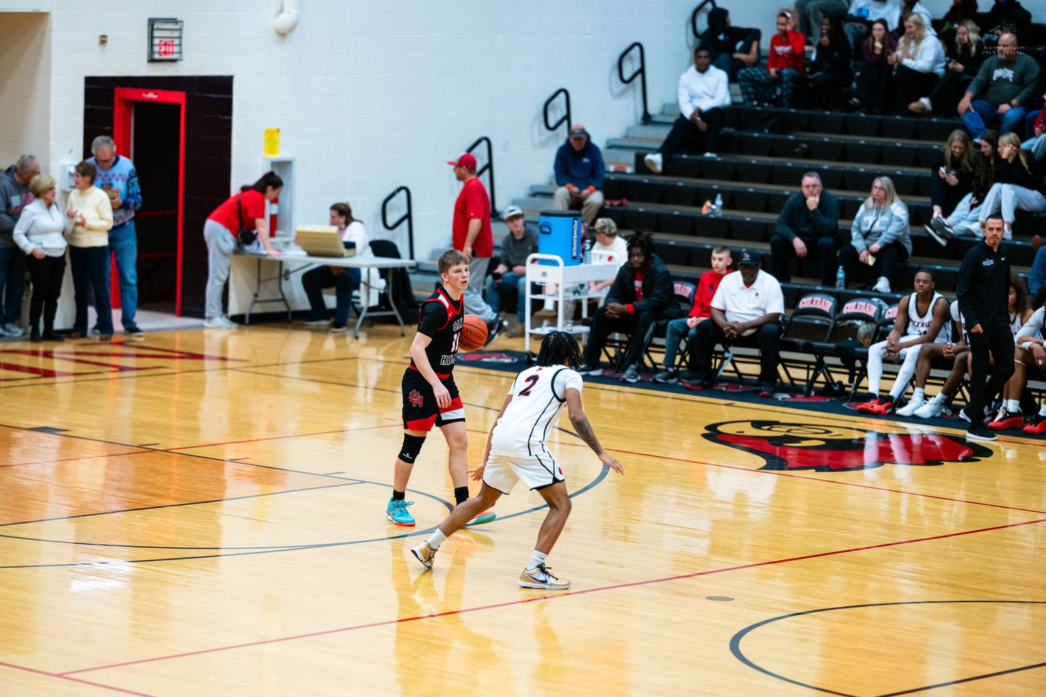 Basketball player in black uniform dribbles while defender guards during high school game.