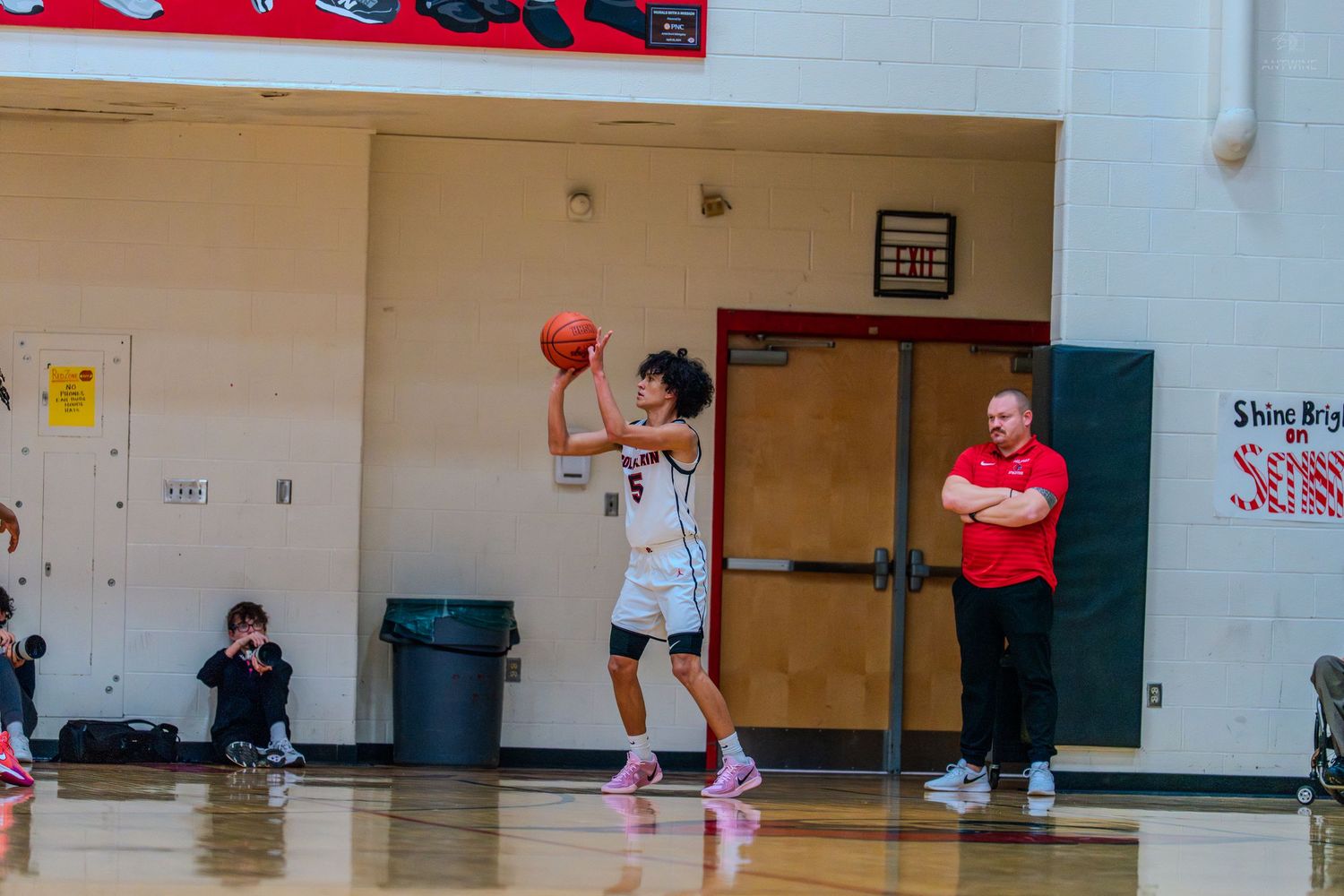 Basketball player #5 prepares to inbound the ball while a coach watches during a high school game.