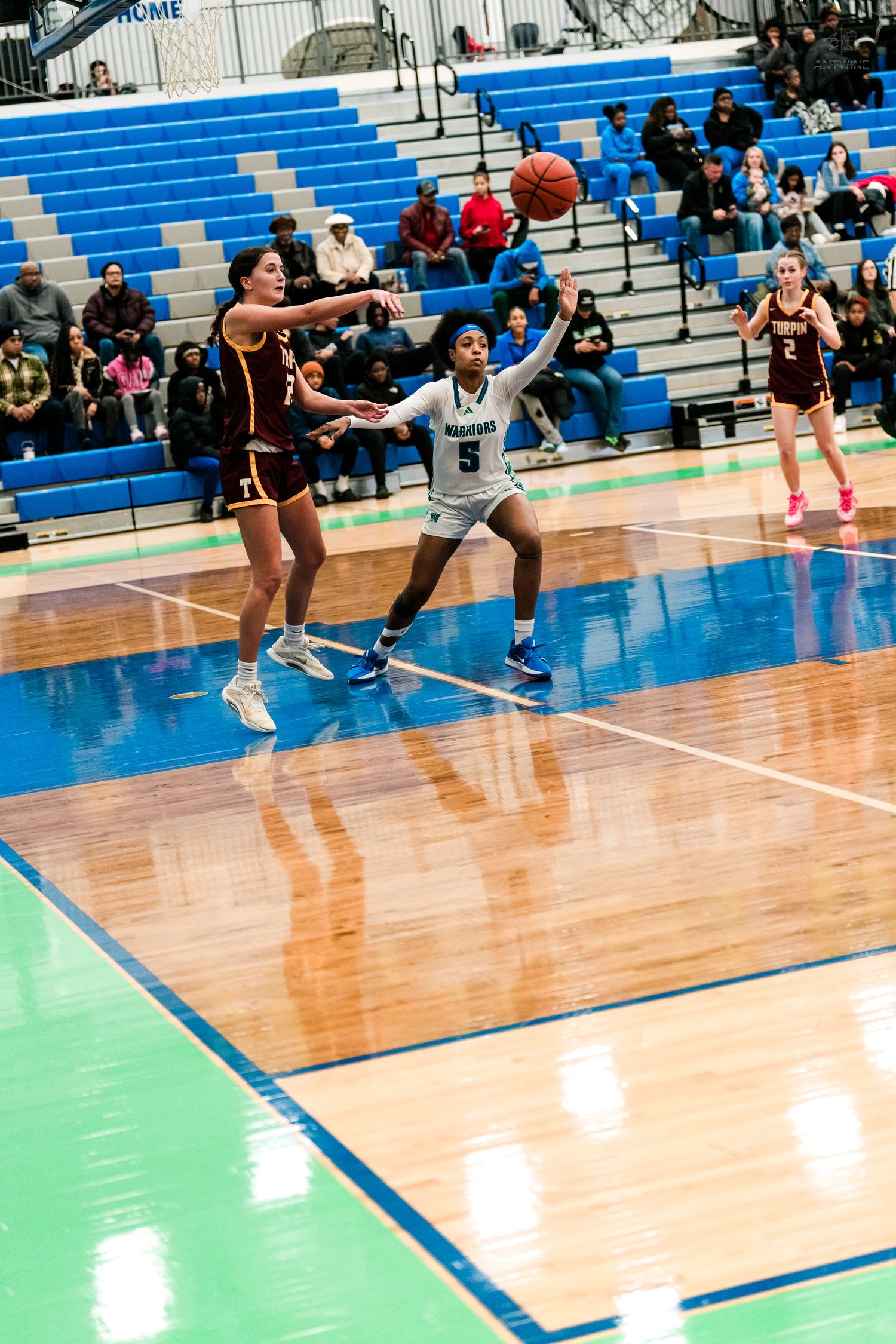 Girls basketball player #5 in white uniform defends against opponent during indoor high school game.