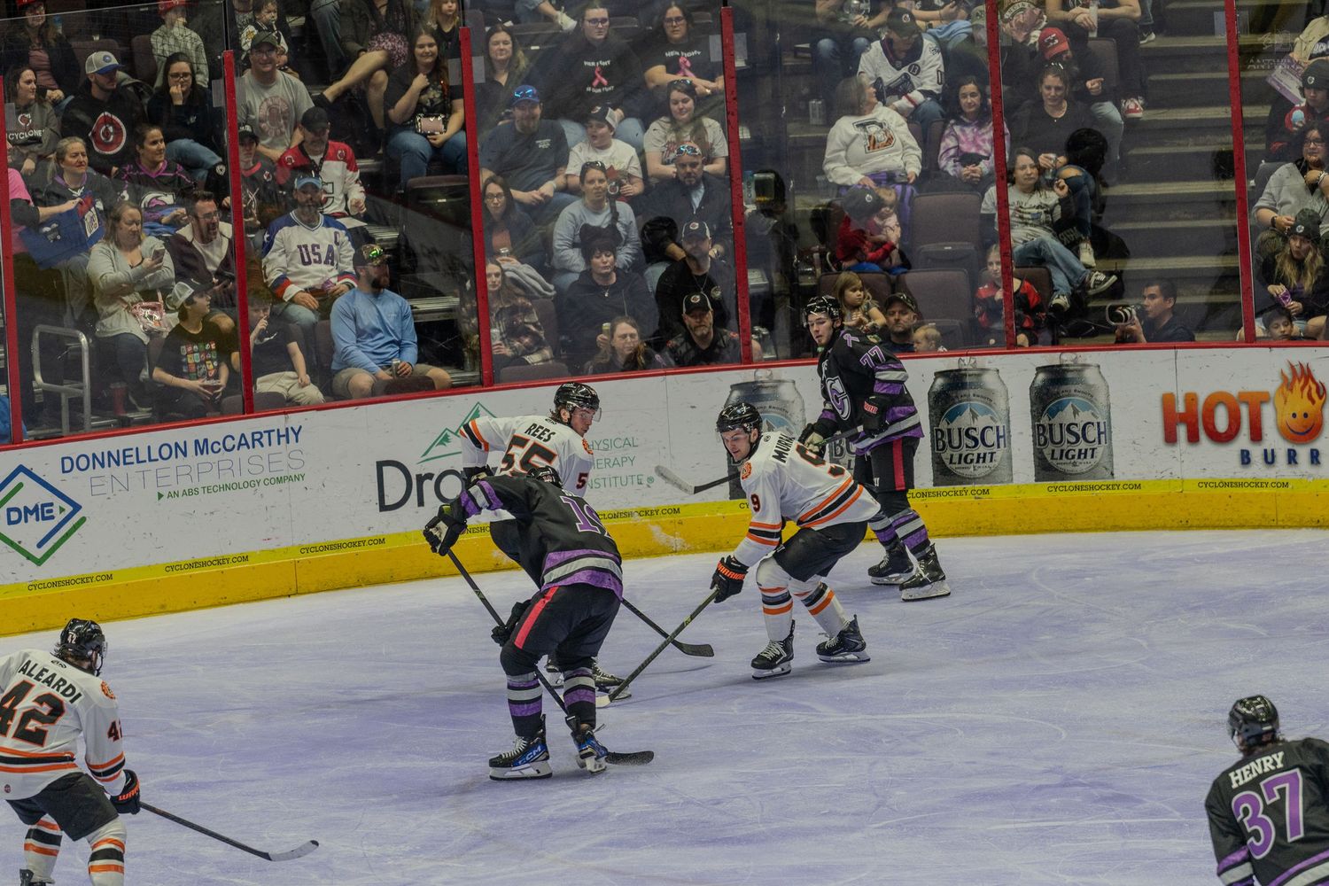 Ice hockey players battle for puck control at center ice during a competitive indoor arena game.