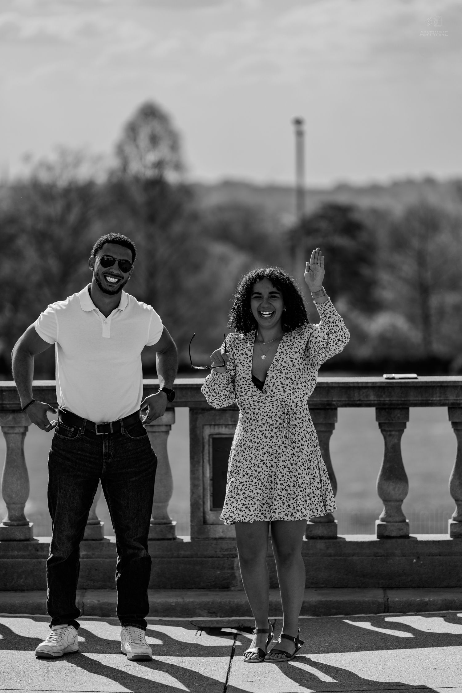 Black and white image of a couple smiling on a stone terrace, woman raising her hand joyfully.