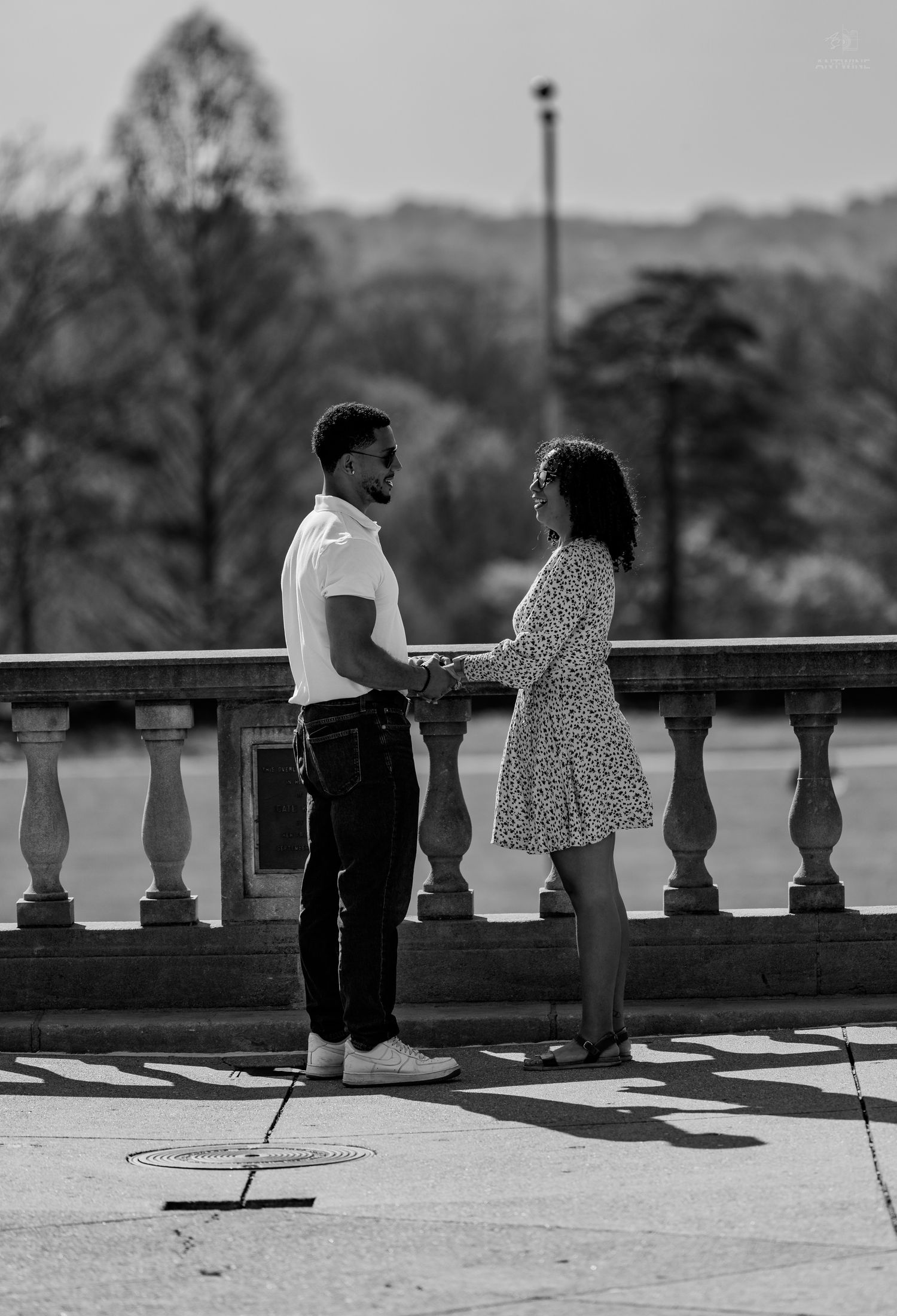 Black and white image of couple holding hands on decorative stone balustrade in outdoor setting.