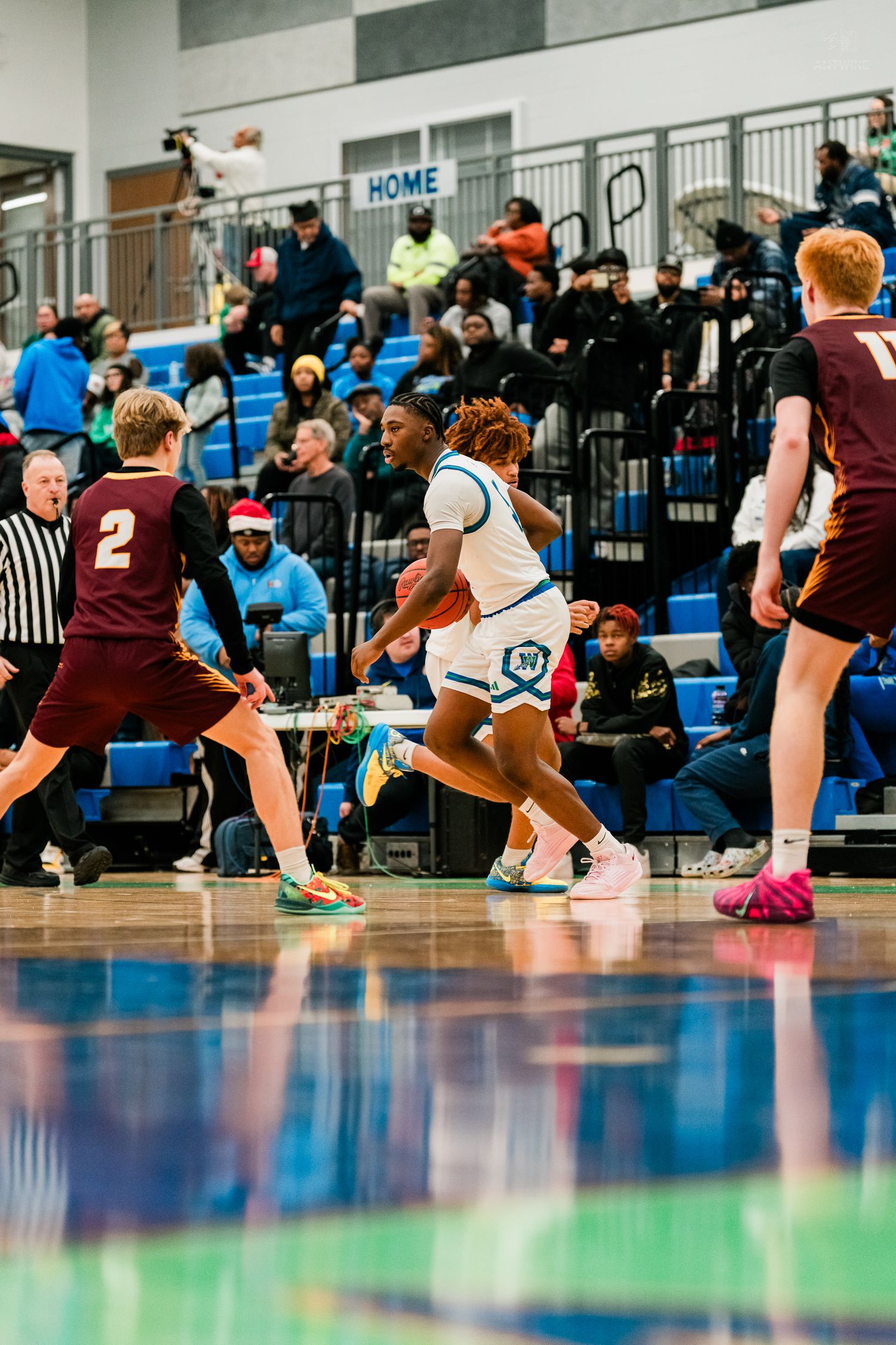Warriors basketball player dribbles upcourt between two maroon-uniformed defenders before a packed home crowd.
