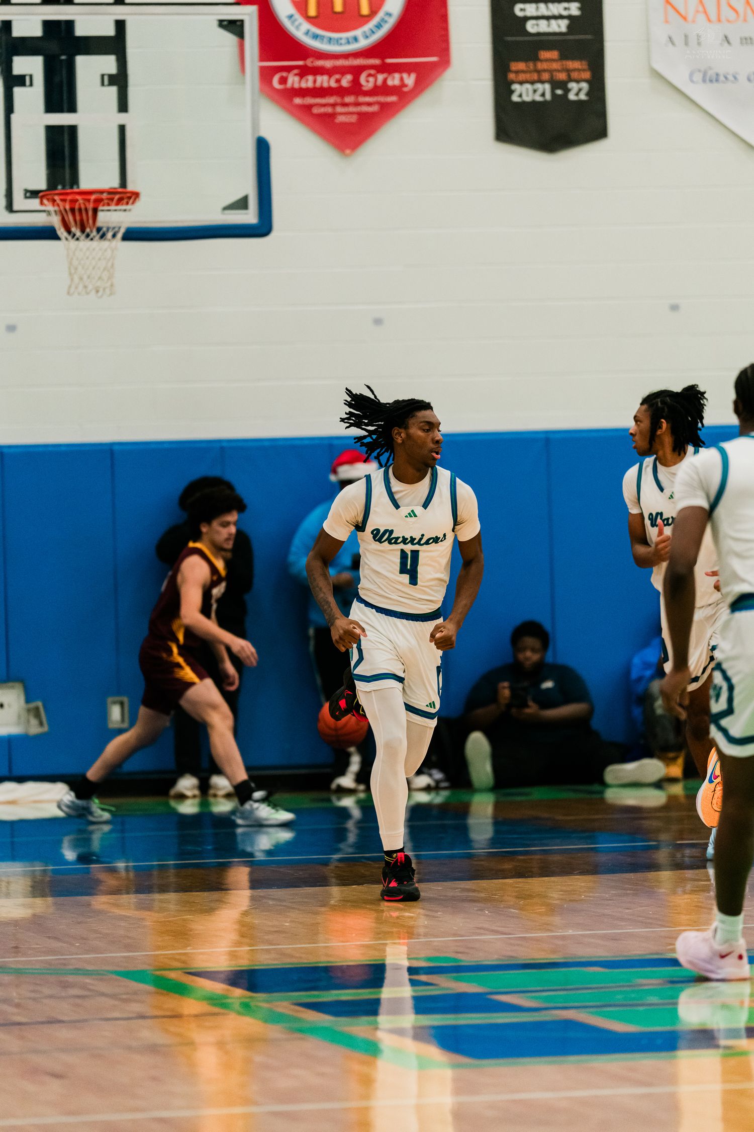 Player #4 in a Warriors uniform jogs upcourt during a high school basketball game at Winton Woods gym.