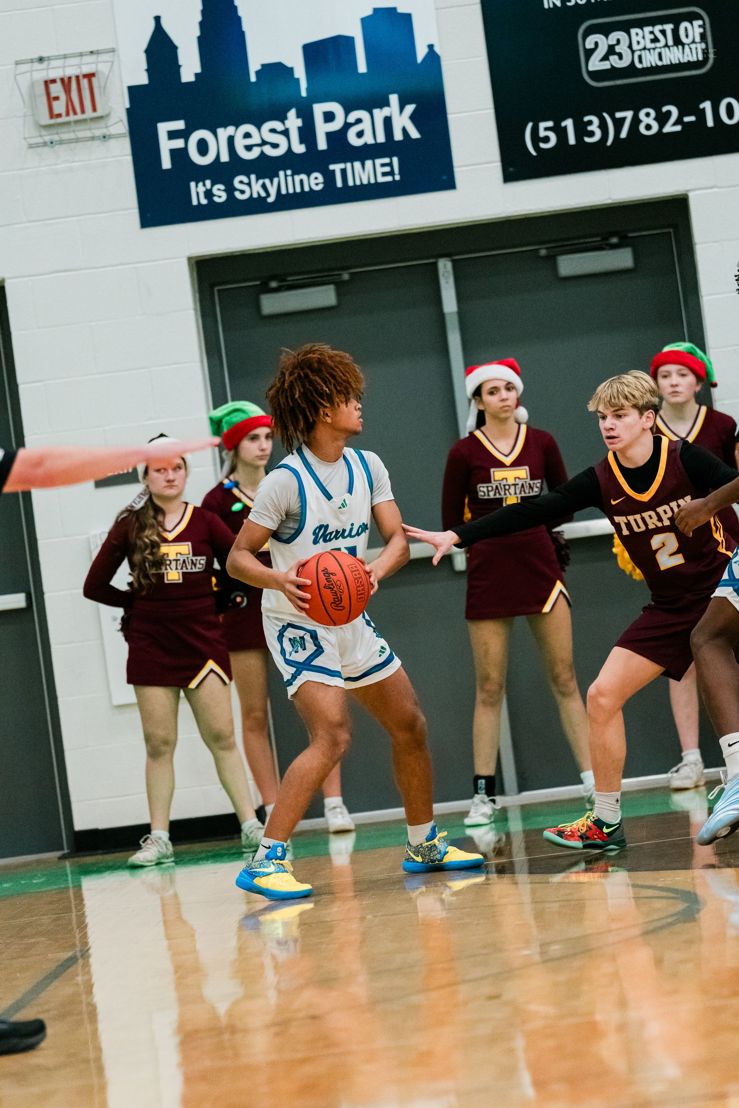 Forest Park gym hosts a holiday basketball game as a Turpin player defends against a Nexus player with cheerleaders.