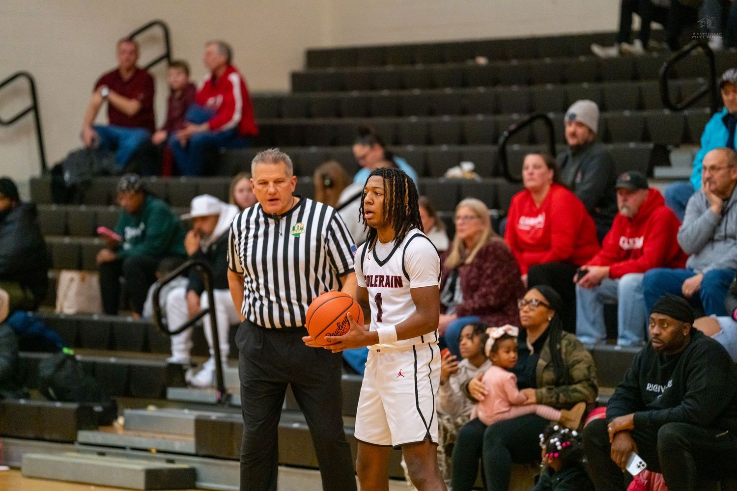 High school basketball player receives inbound pass instructions from a referee near the sideline.
