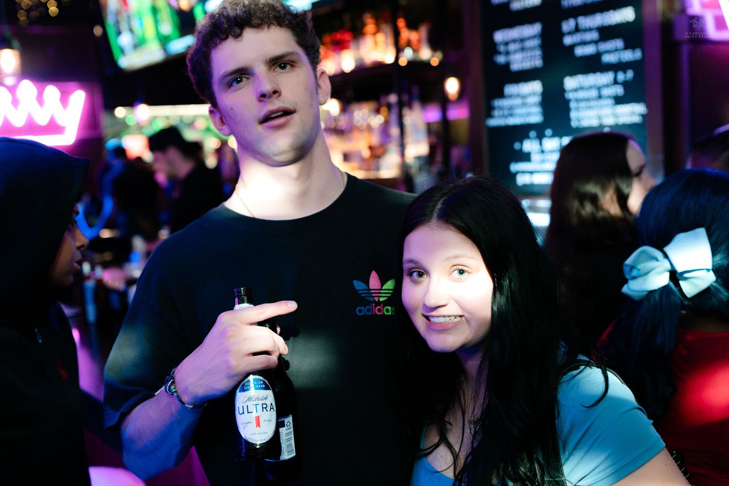 Young couple posing together at a vibrant nightclub with neon bar lights.