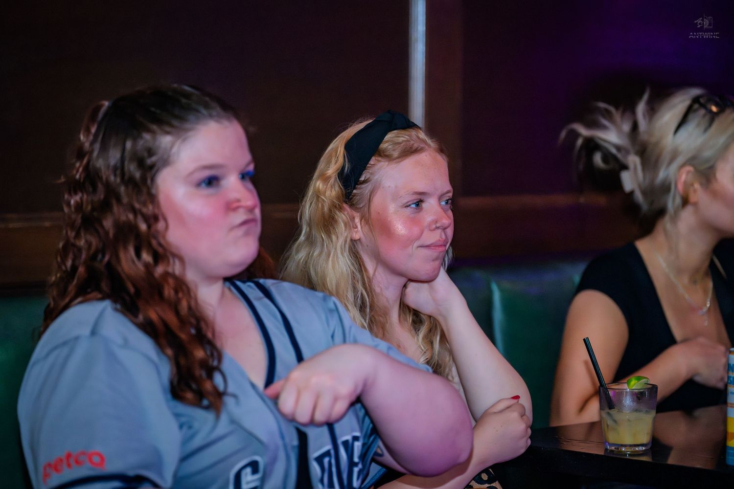 Two women watch attentively while seated at a dimly lit sports bar event.