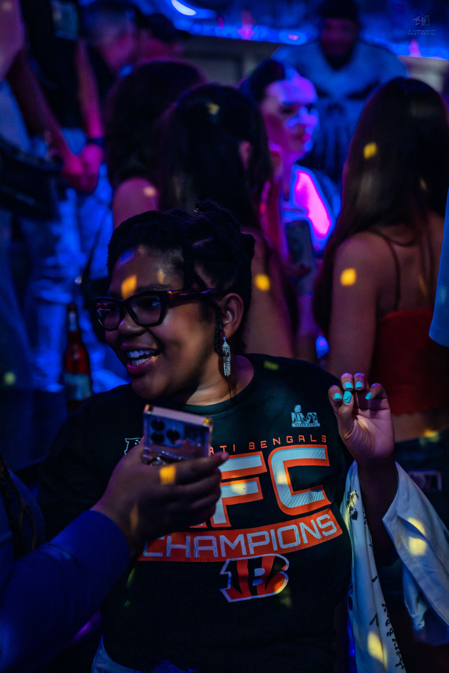 Smiling woman in Cincinnati Bengals AFC Champions shirt dancing at a neon-lit nightclub party.