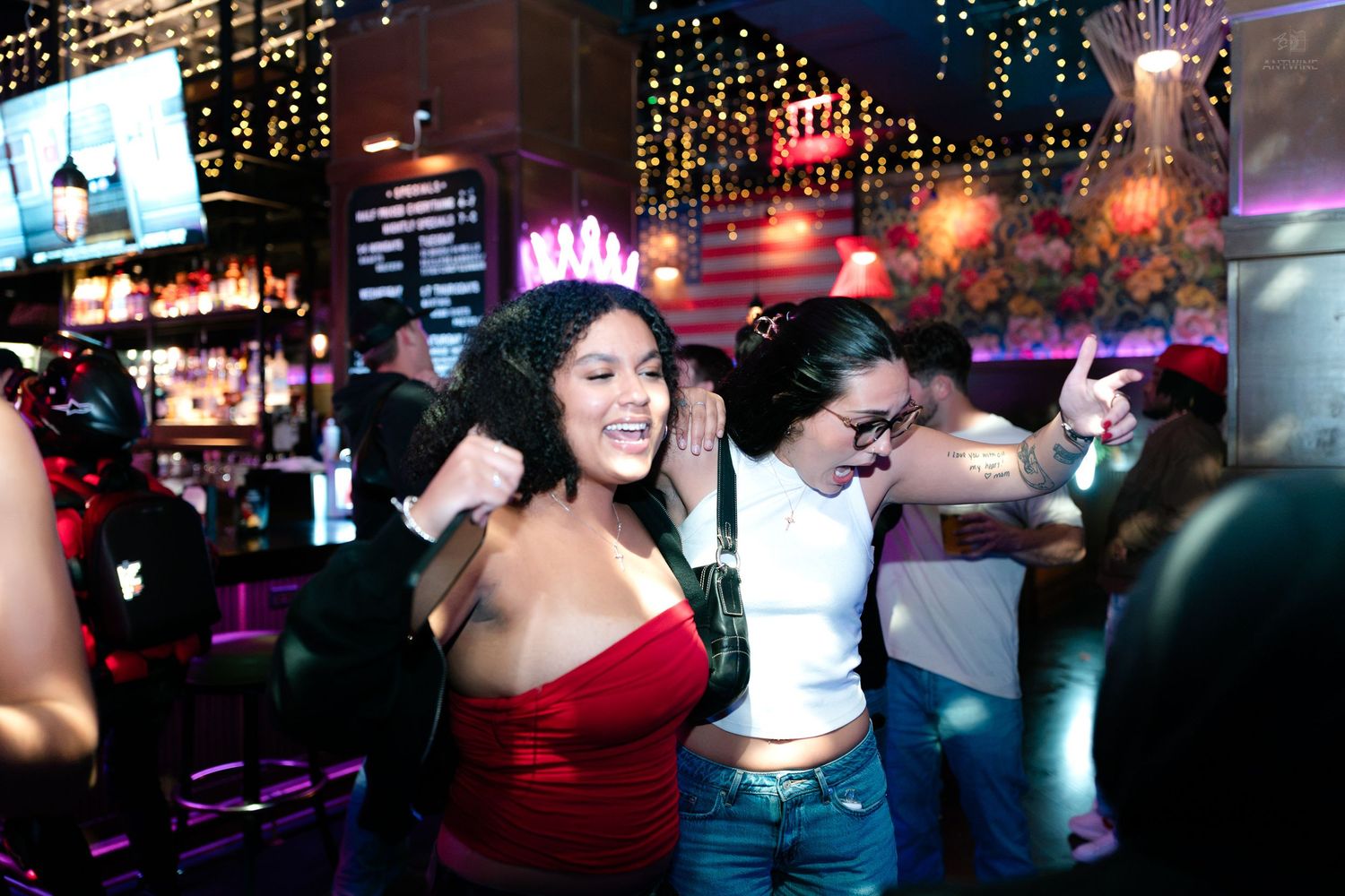 Women dancing and having fun at a vibrant nightclub with neon lights and festive decor.