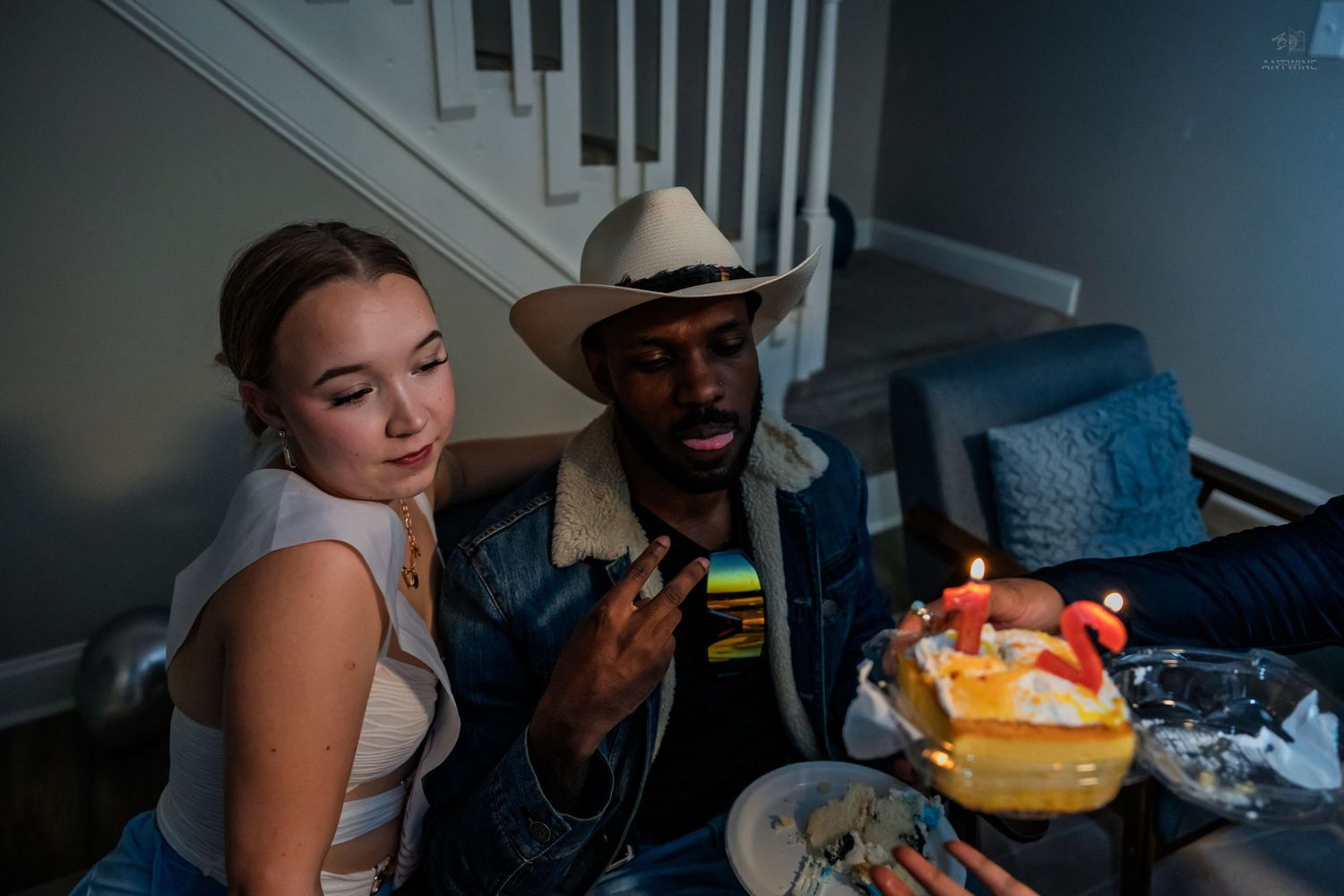 Woman and man in cowboy hat sitting together examining a small birthday cake with lit candles.