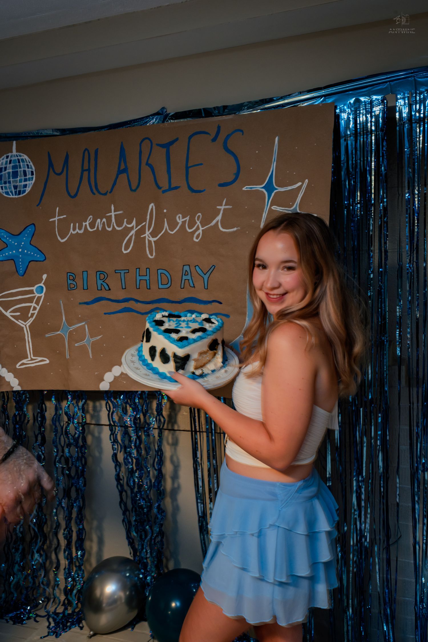 Young woman smiling while holding blue heart-shaped birthday cake at Malarie's twenty-first birthday party celebration.