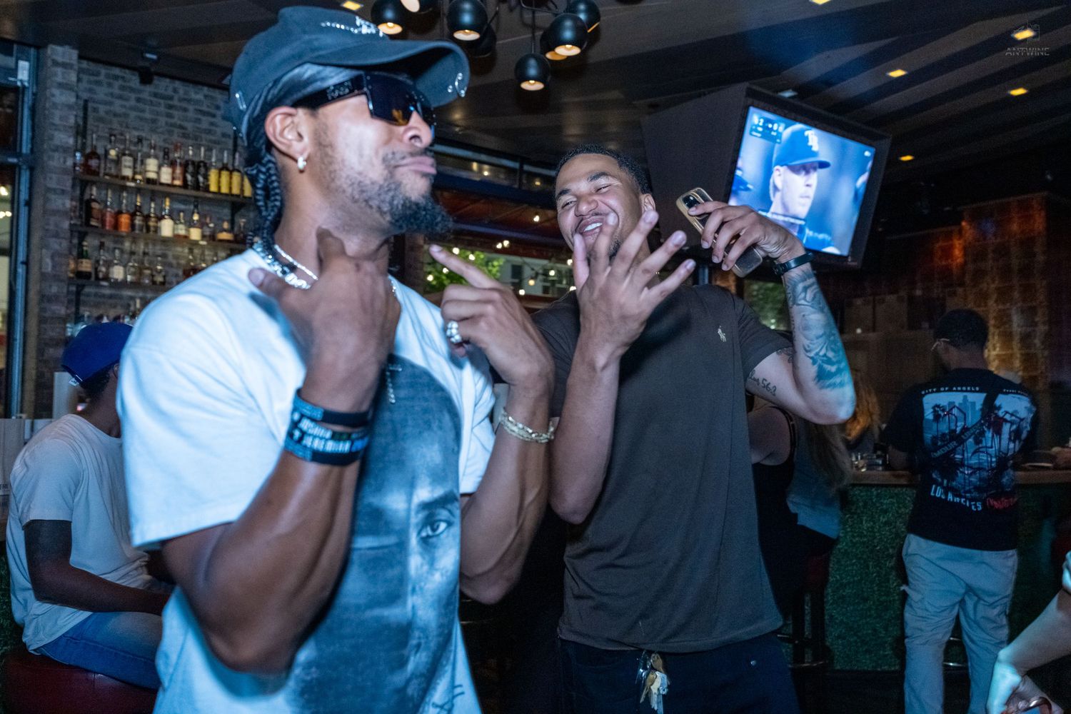 Two men laughing and gesturing animatedly together inside a lively bar setting.
