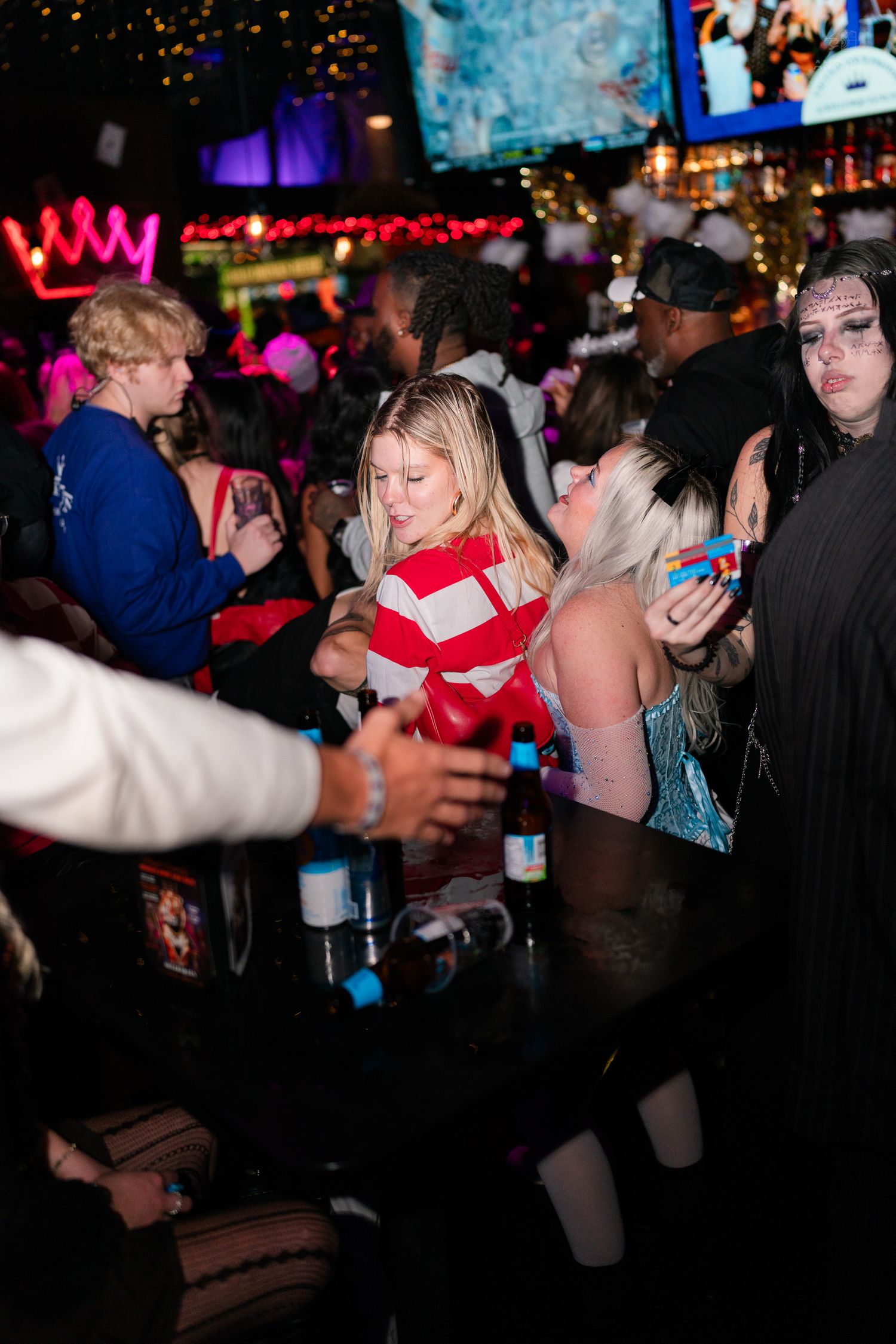 Crowd of Halloween costume party guests gathering around a bar inside a festively lit nightclub.