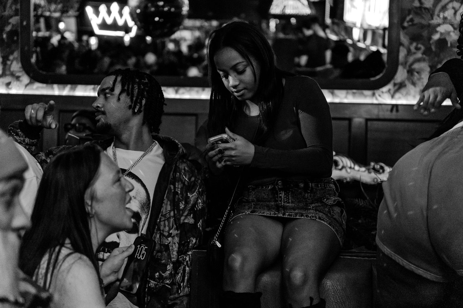 Three people in intimate conversation at a dimly lit bar booth, captured in black and white photography.