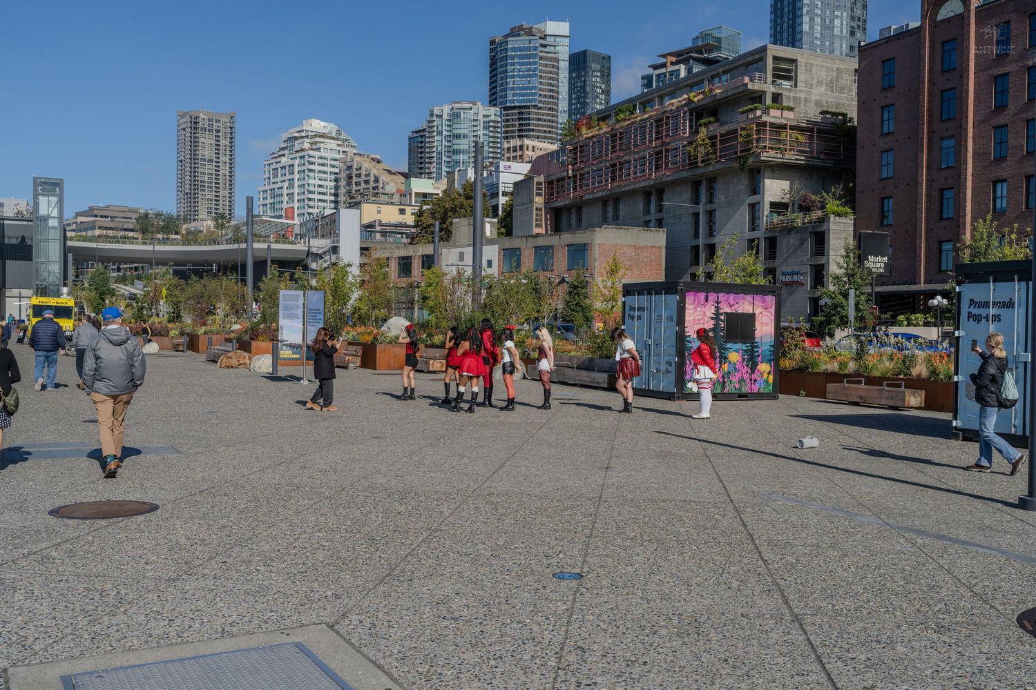 Visitors explore an open waterfront plaza in Seattle with city skyline and modern buildings in background.