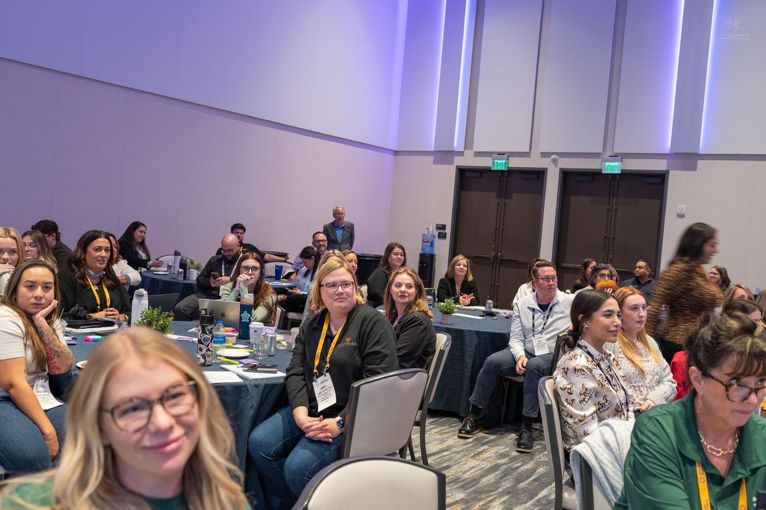 Large group of engaged conference attendees seated at round tables in a modern convention hall.