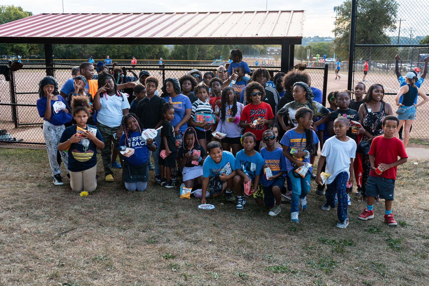 Large group of children posing together outdoors at a baseball field during a community youth sports event.