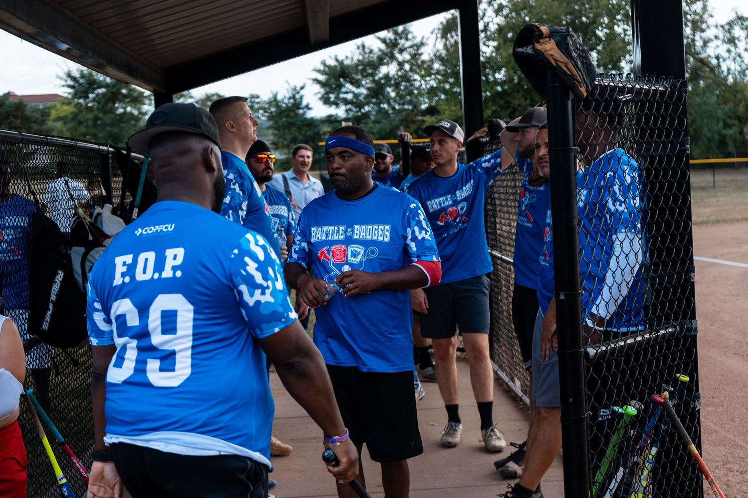 Team members in blue Battle of Badges jerseys celebrate in dugout during charity softball game.