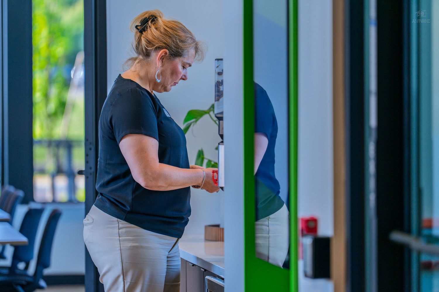 Woman in black shirt using a vending machine or kiosk in a modern building interior.