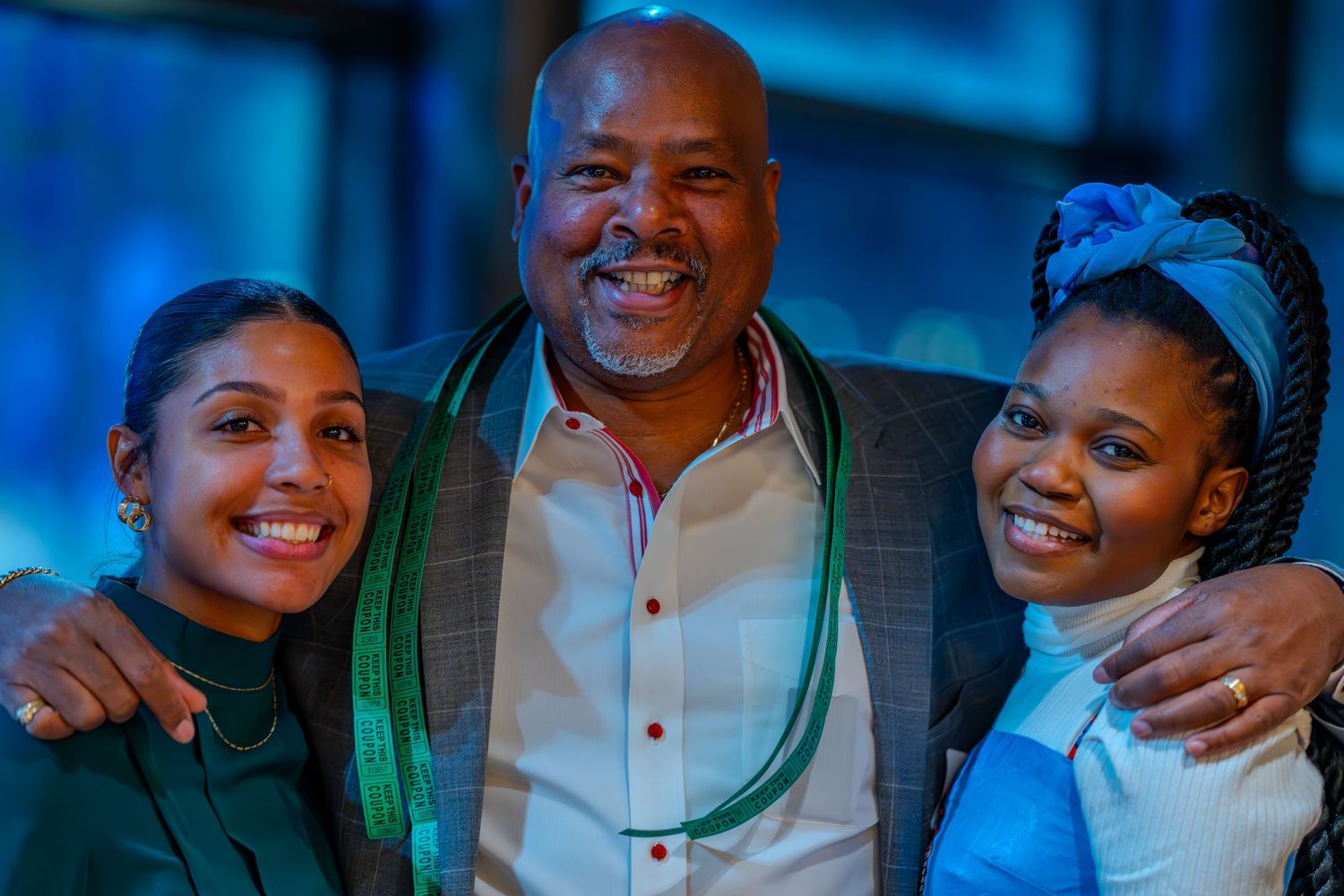 A smiling man with two women posing together at a formal event, wearing elegant attire with green accessories.
