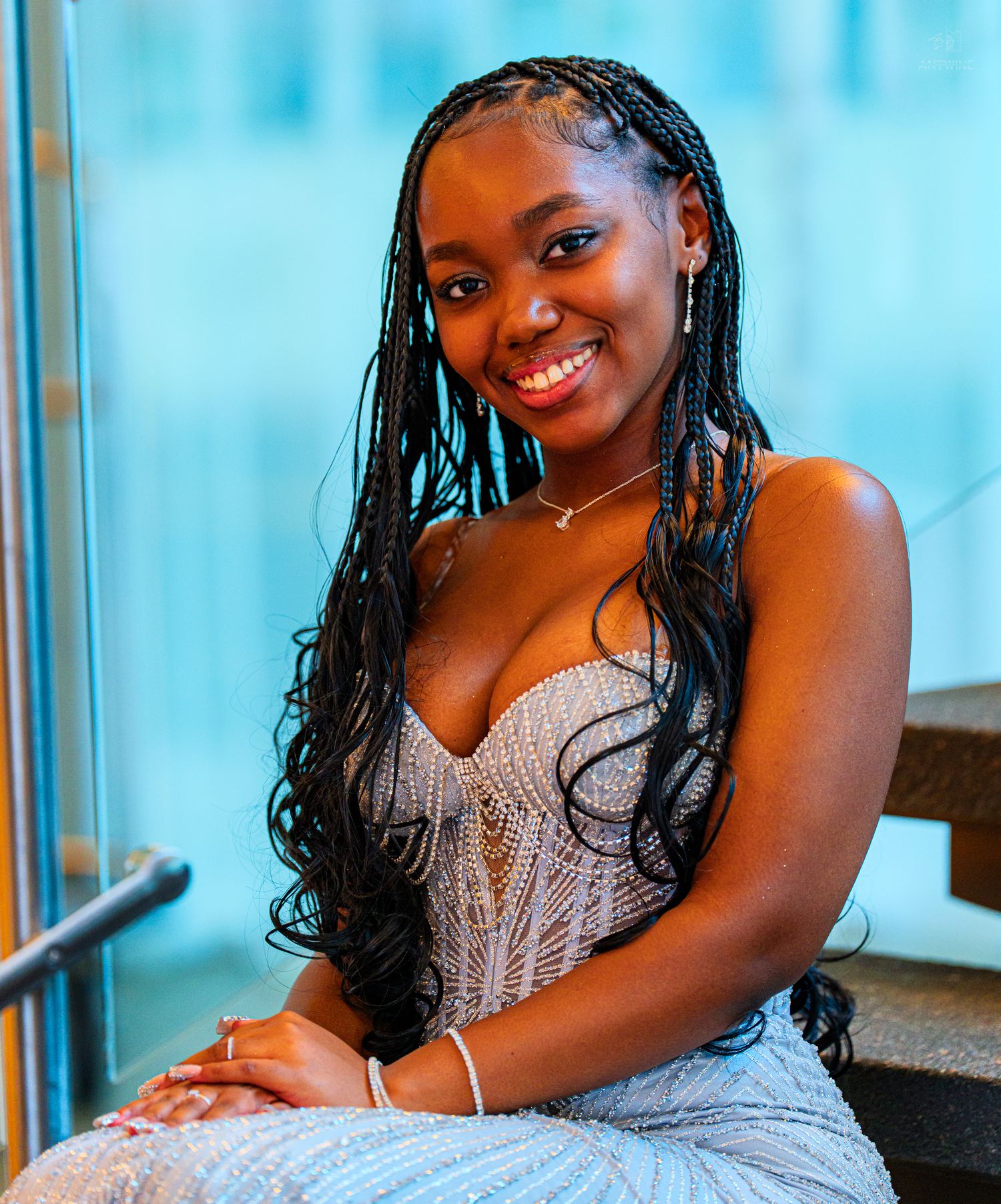 Young woman in silver beaded gown smiling warmly while seated on modern staircase.